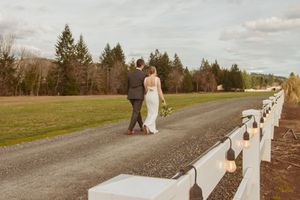 A couple walks down a gravel path lined with glowing lights on white fencing at dusk.