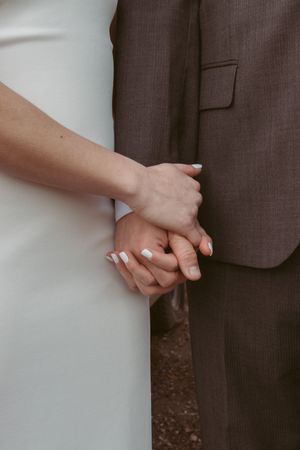 Close up shot of wedding couple holding hands showing suit jacket detailing.