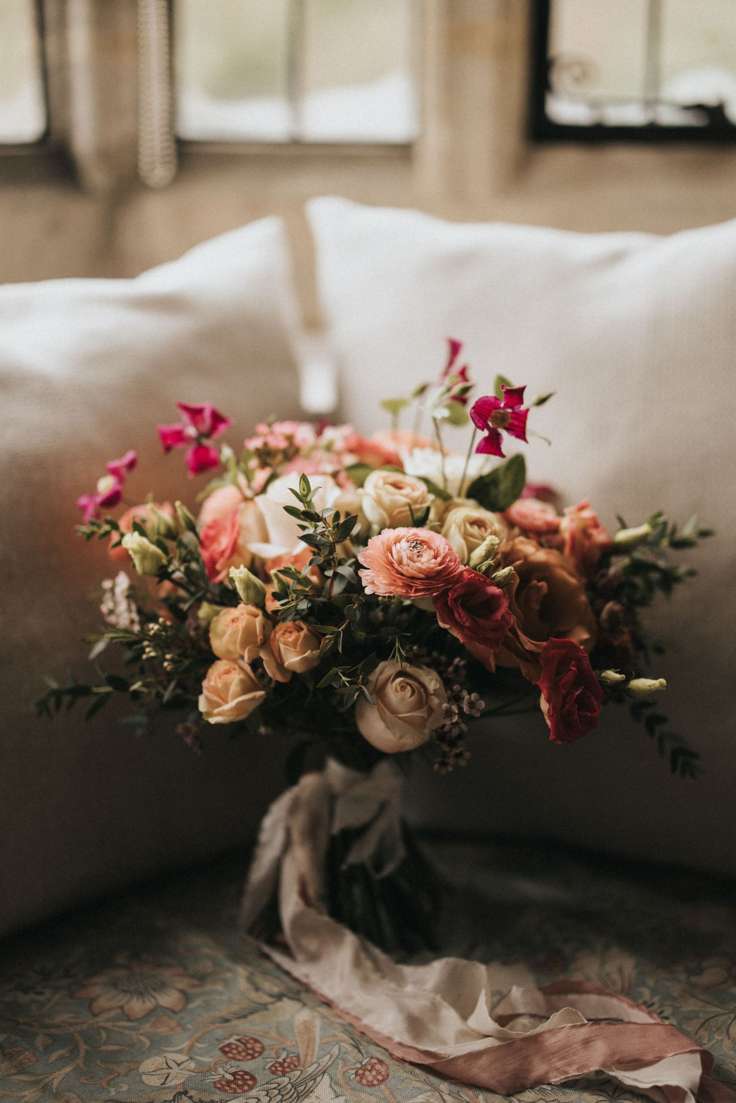 A romantic floral arrangement with peach roses and magenta flowers on a table with flowing fabric.