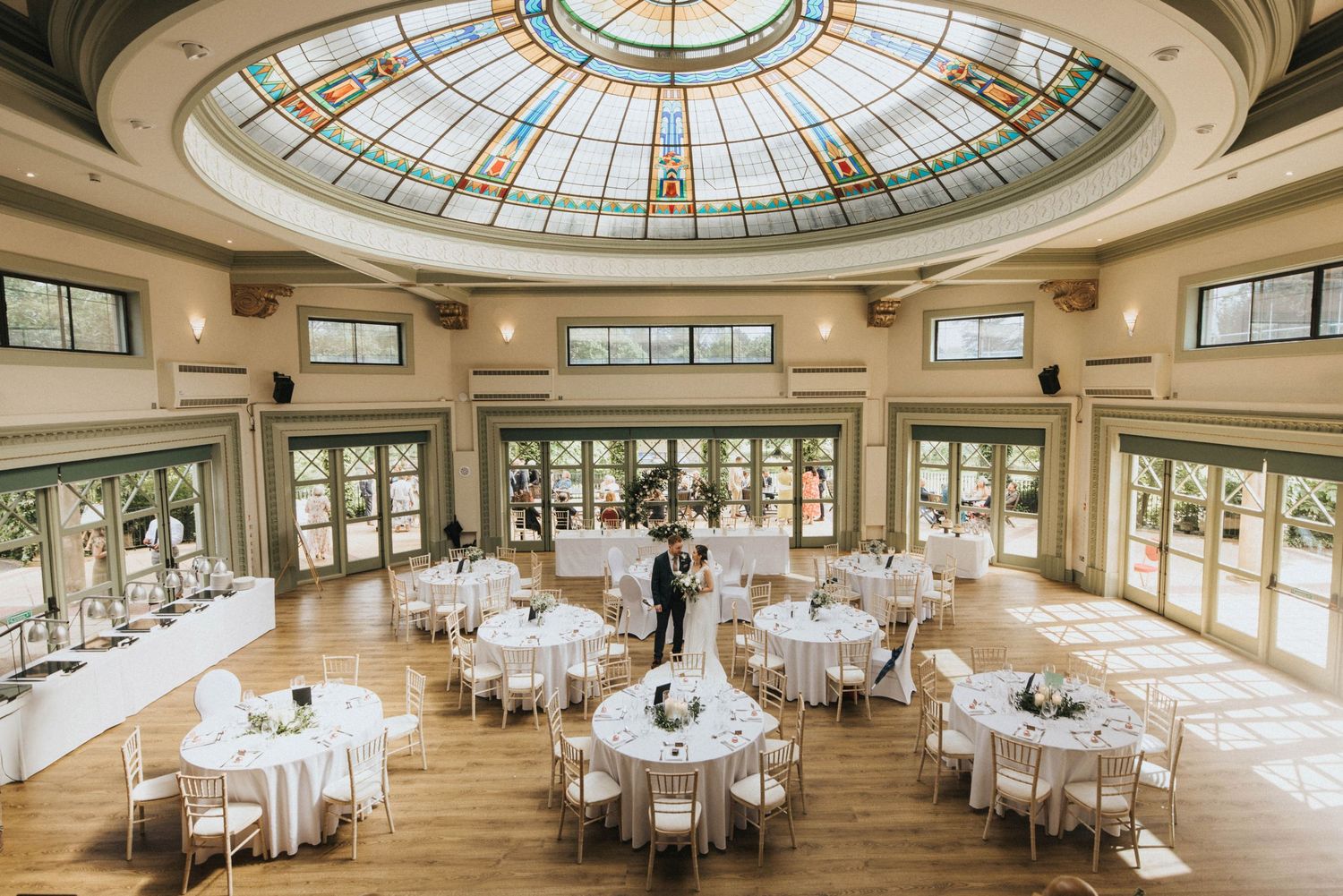 Elegant ballroom with stained glass dome ceiling and circular dining tables set for an elegant event or wedding reception.