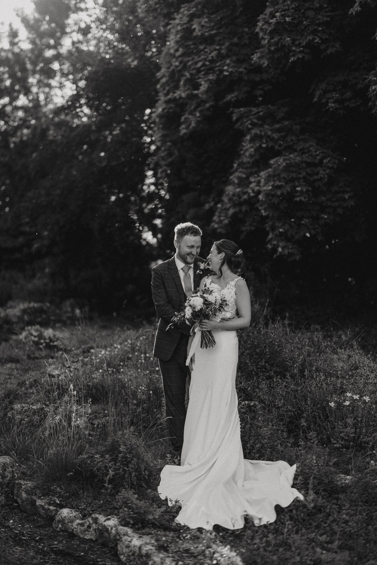 Black and white wedding couple poses romantically in meadow surrounded by wildflowers.