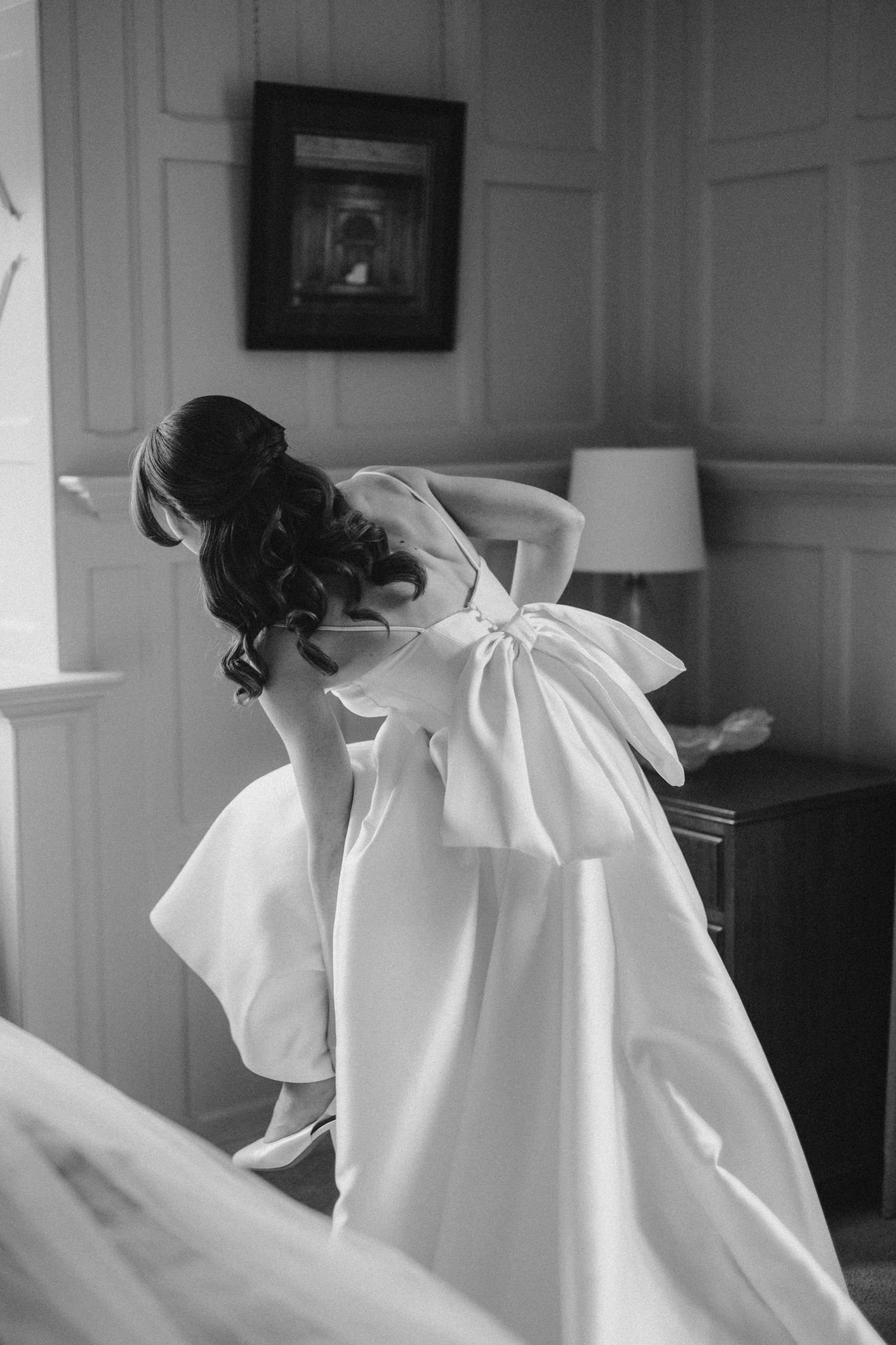 A black and white photograph shows a figure in a flowing white dress leaning down in dramatic motion.