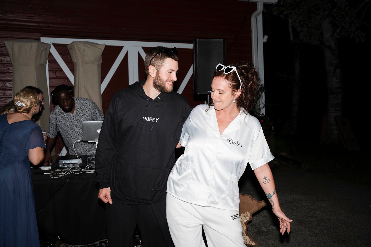 People in white clothing walking through a dark space at what appears to be a nighttime event or venue.