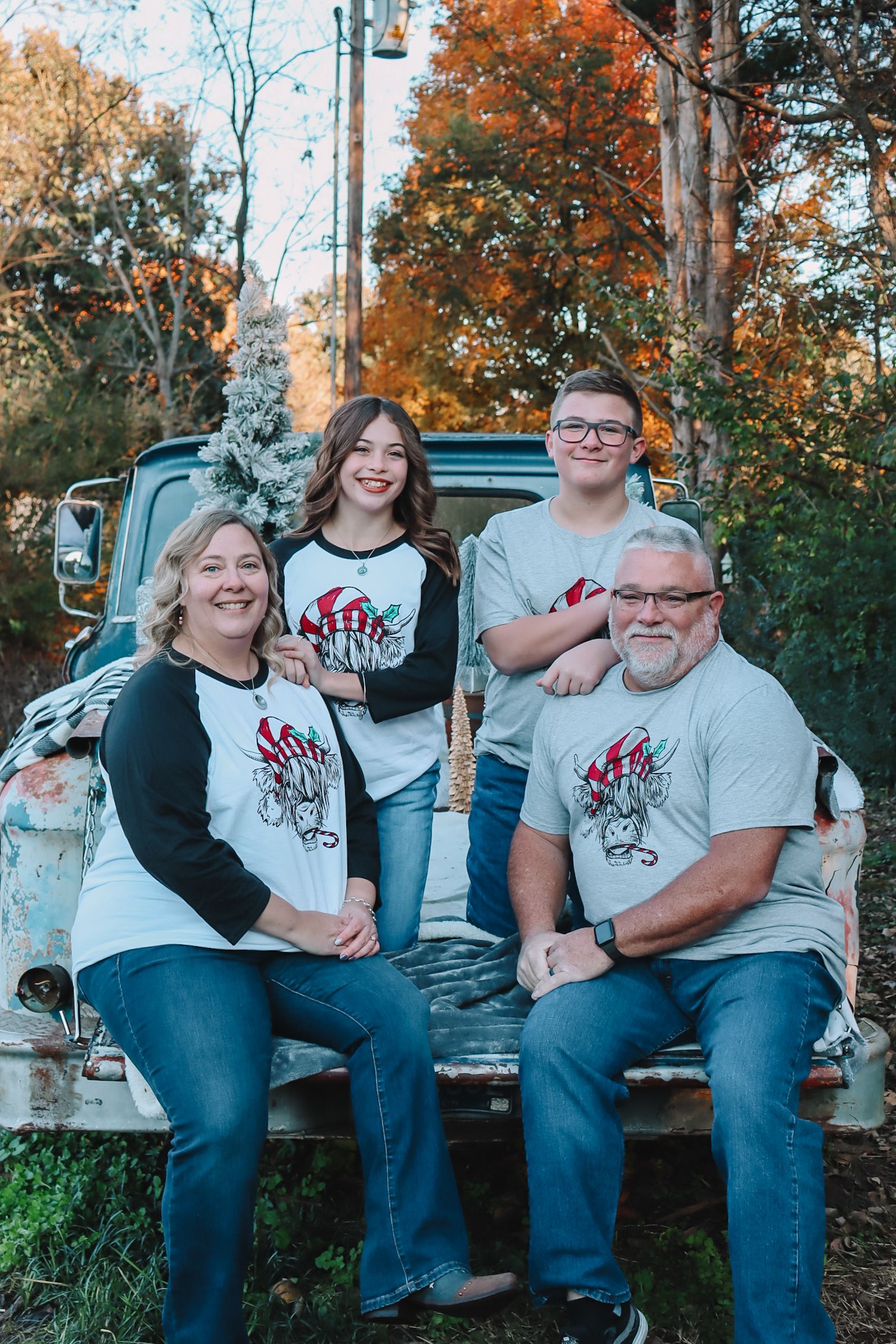 A family wearing matching white t-shirts sits together on a rustic wooden fence during an autumn photo session.