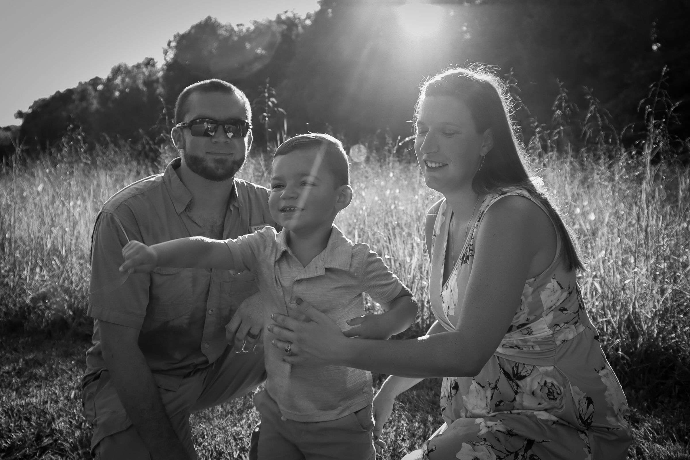 A family shares a happy moment together in a sunlit meadow captured in black and white photography.