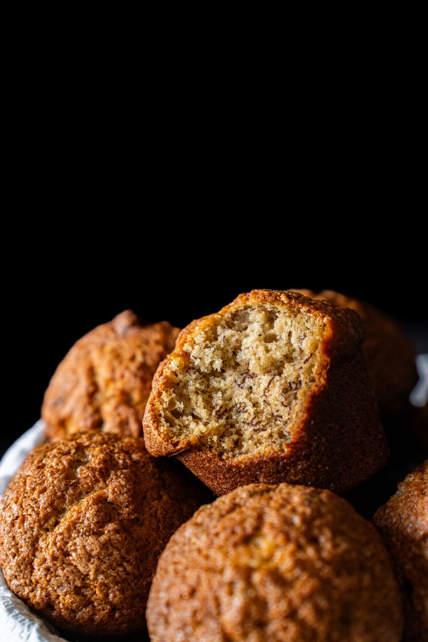 Bowl full of banana muffins in front of a dark background.
