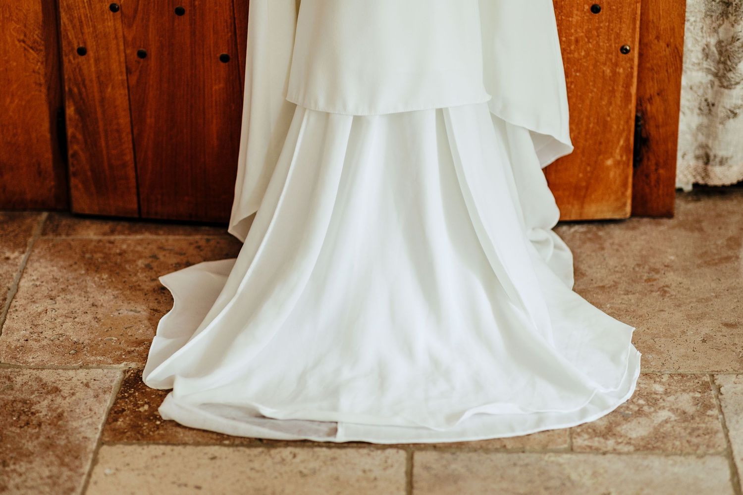 Bottom portion of an elegant white wedding dress flowing across terracotta tile flooring.