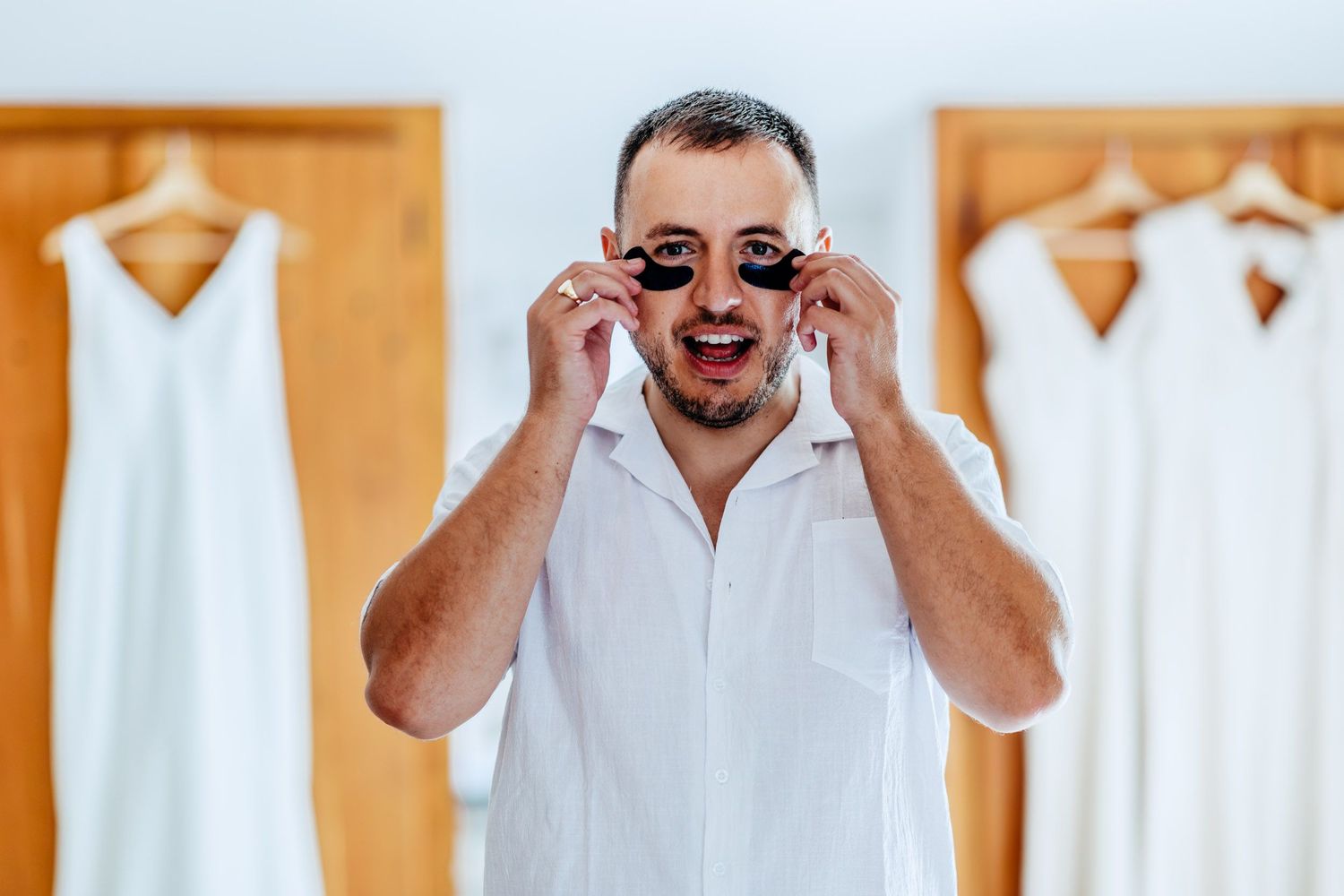 A person in a white dress shirt adjusts their glasses while looking at a mirror reflection during a wedding day preparation.