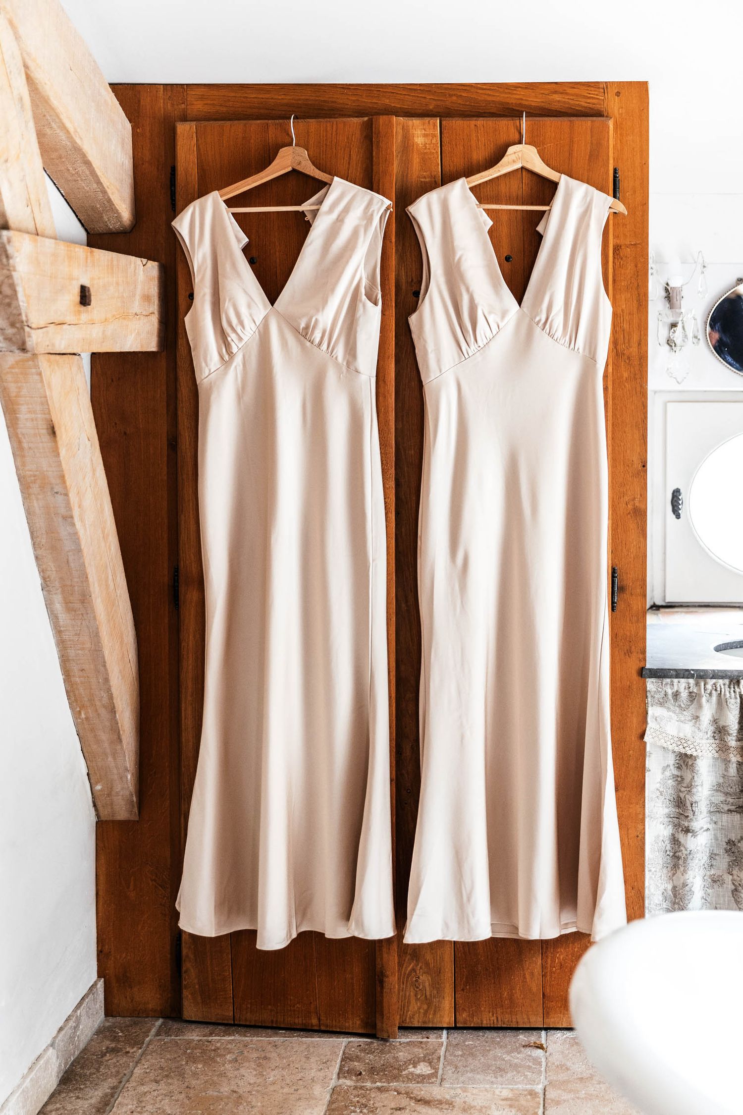 White sleeveless bridesmaid dresses hanging in a row on wooden hangers against a rustic wall.