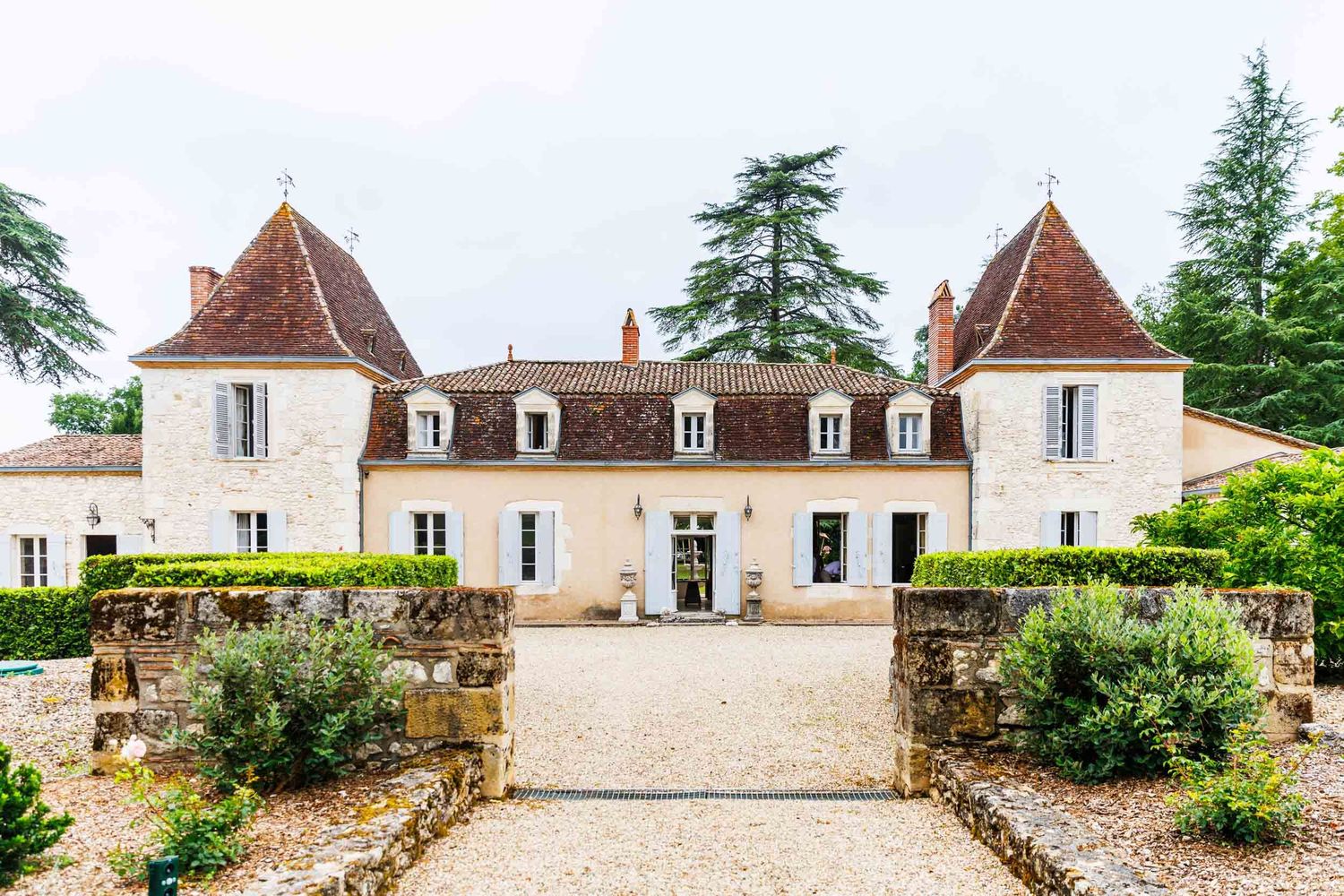 A majestic French chateau with twin turrets and white stone facade stands at the end of a gravel driveway in Bordeaux.