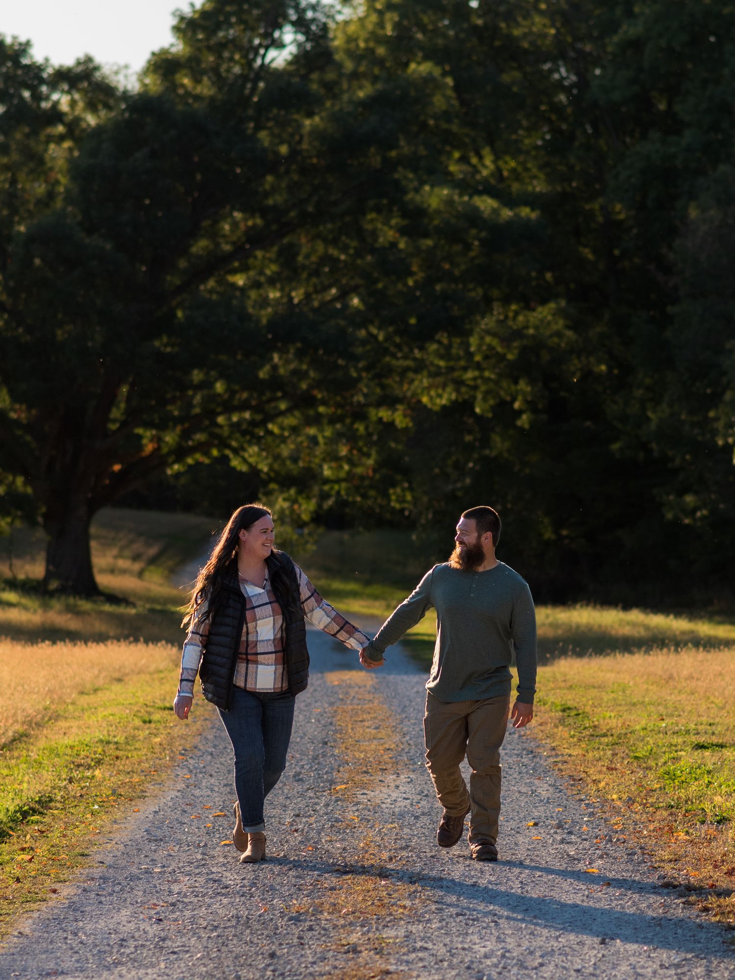 Silhouettes of a couple walking hand in hand down a gravel path at sunset.