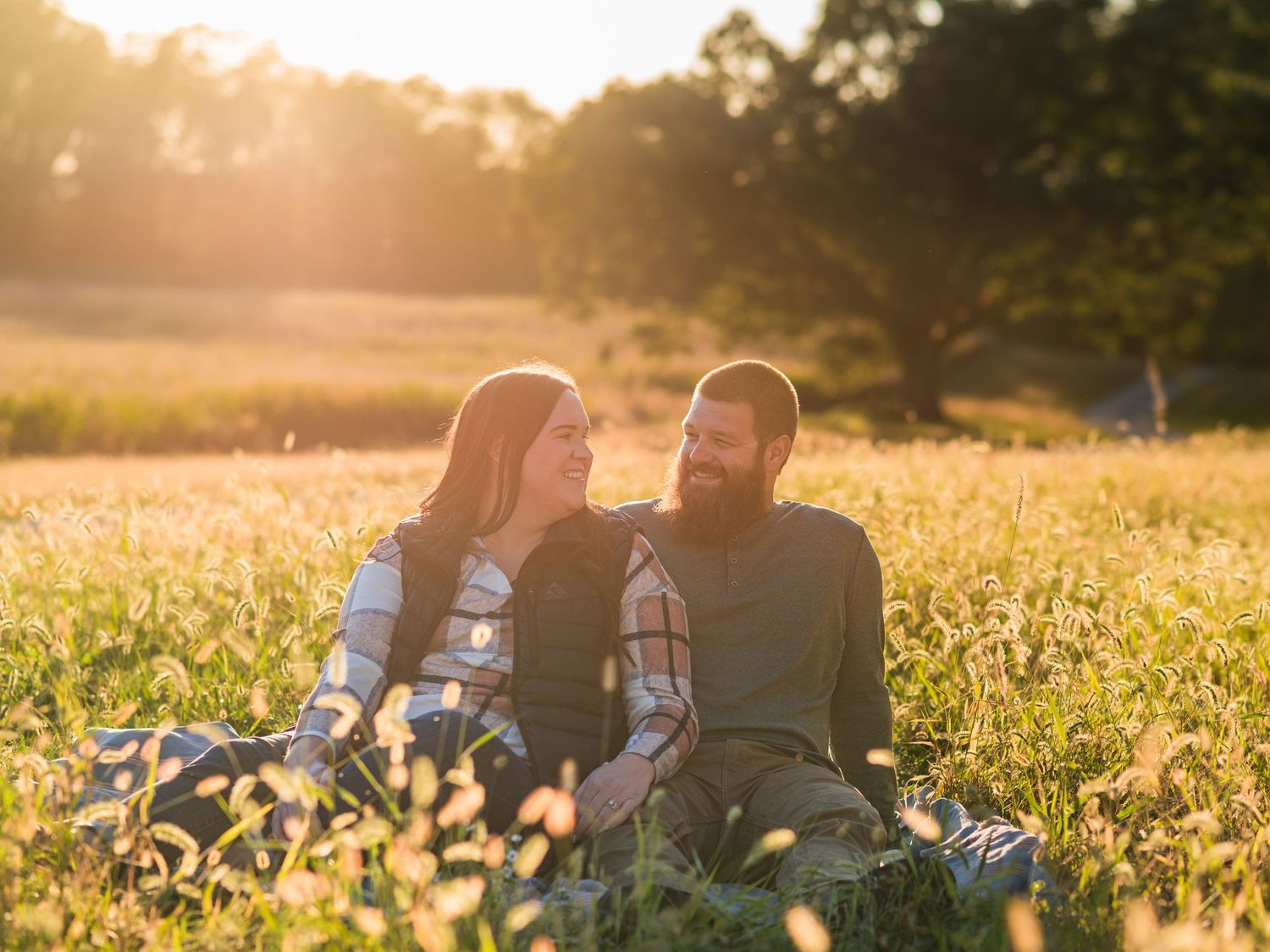 Couple sitting together in a golden wildflower meadow at sunset sharing an intimate moment.