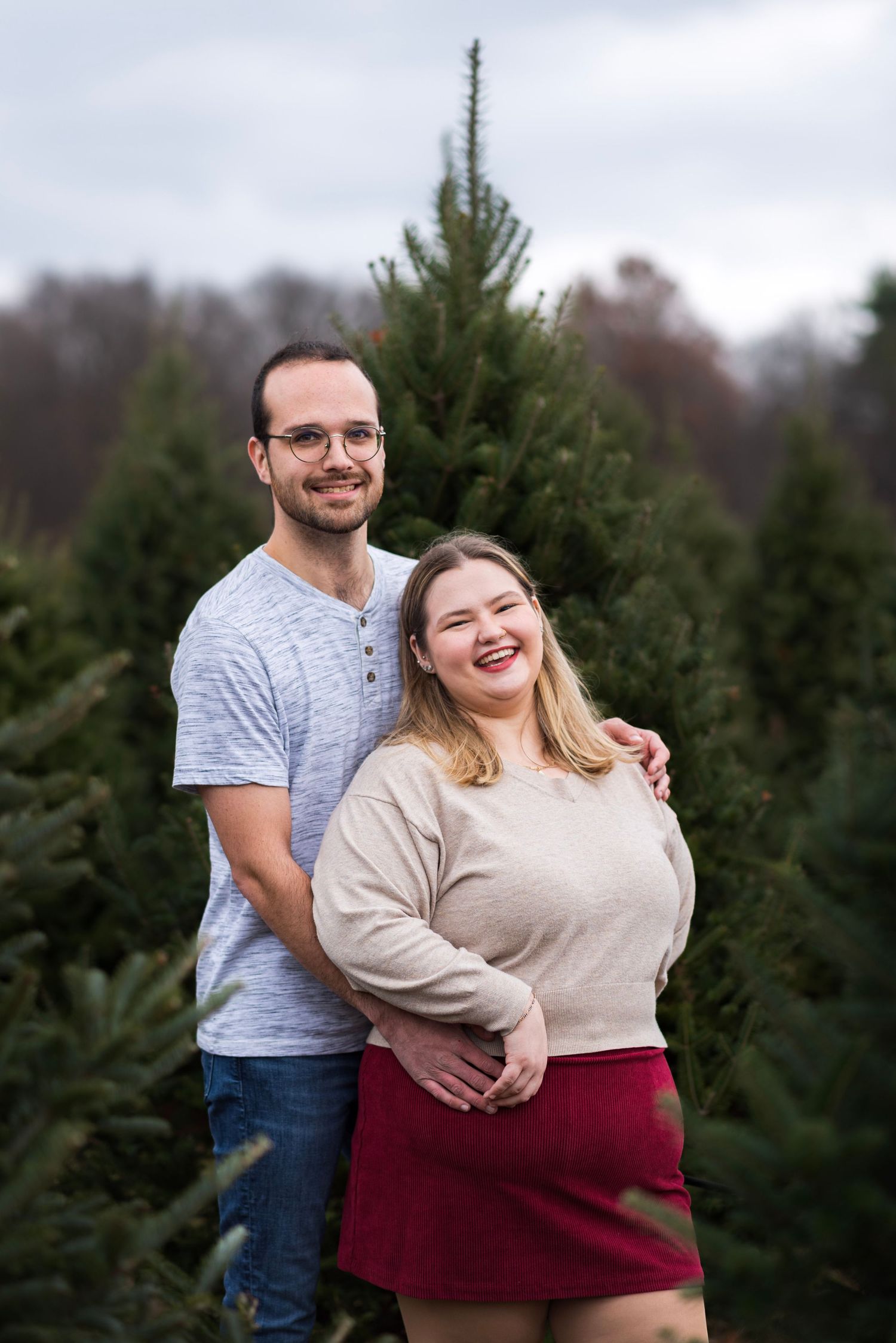 Happy couple embracing at a tree farm surrounded by evergreen trees.