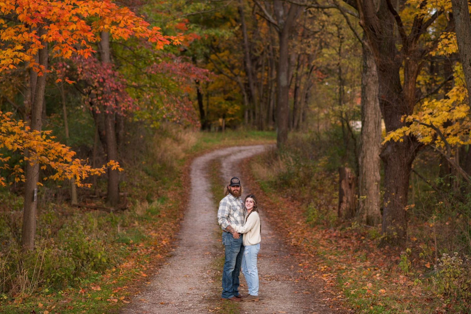 Couple walking down autumn trail surrounded by vibrant fall foliage.