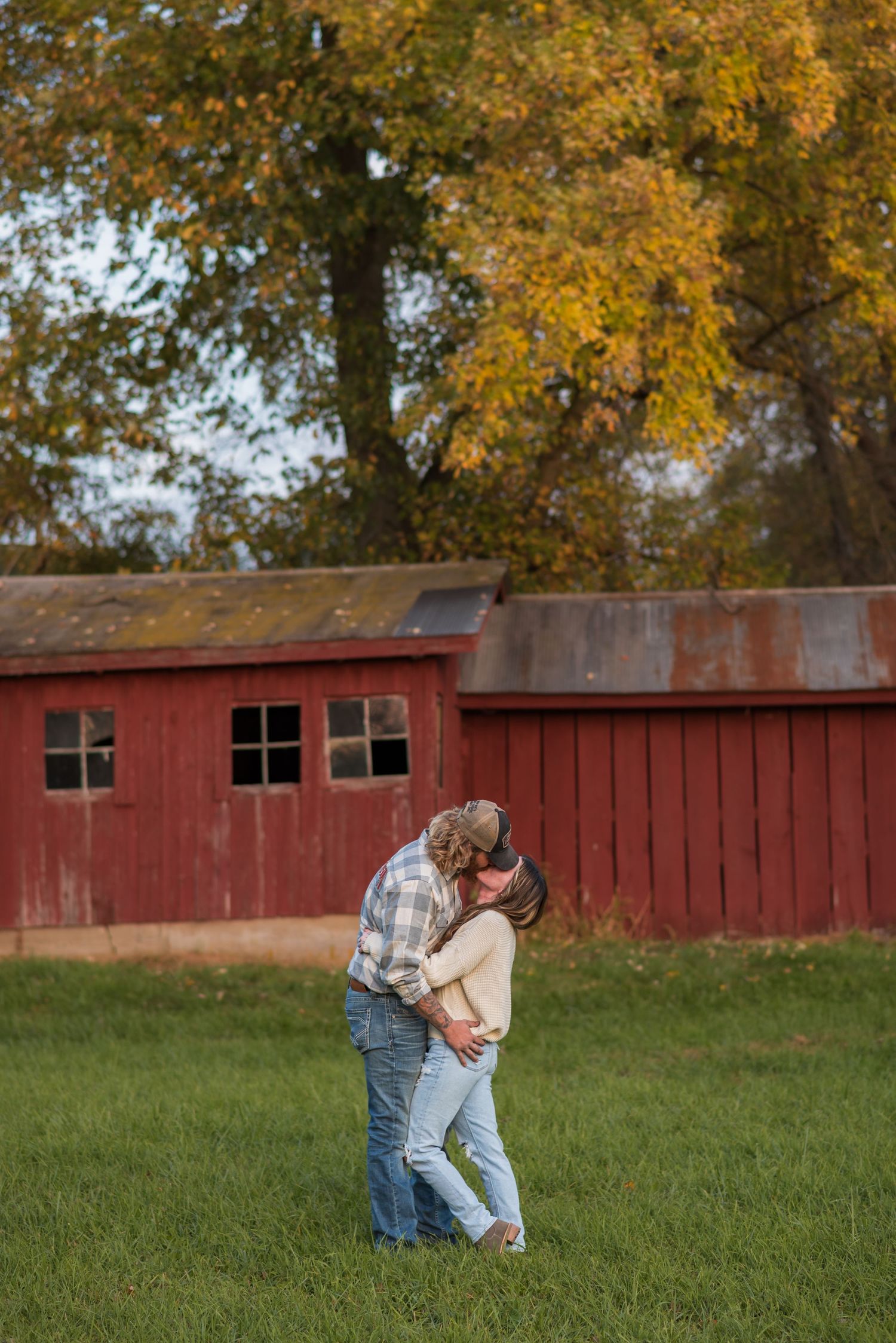 Romantic moment captured in field with red barn in background during fall season.