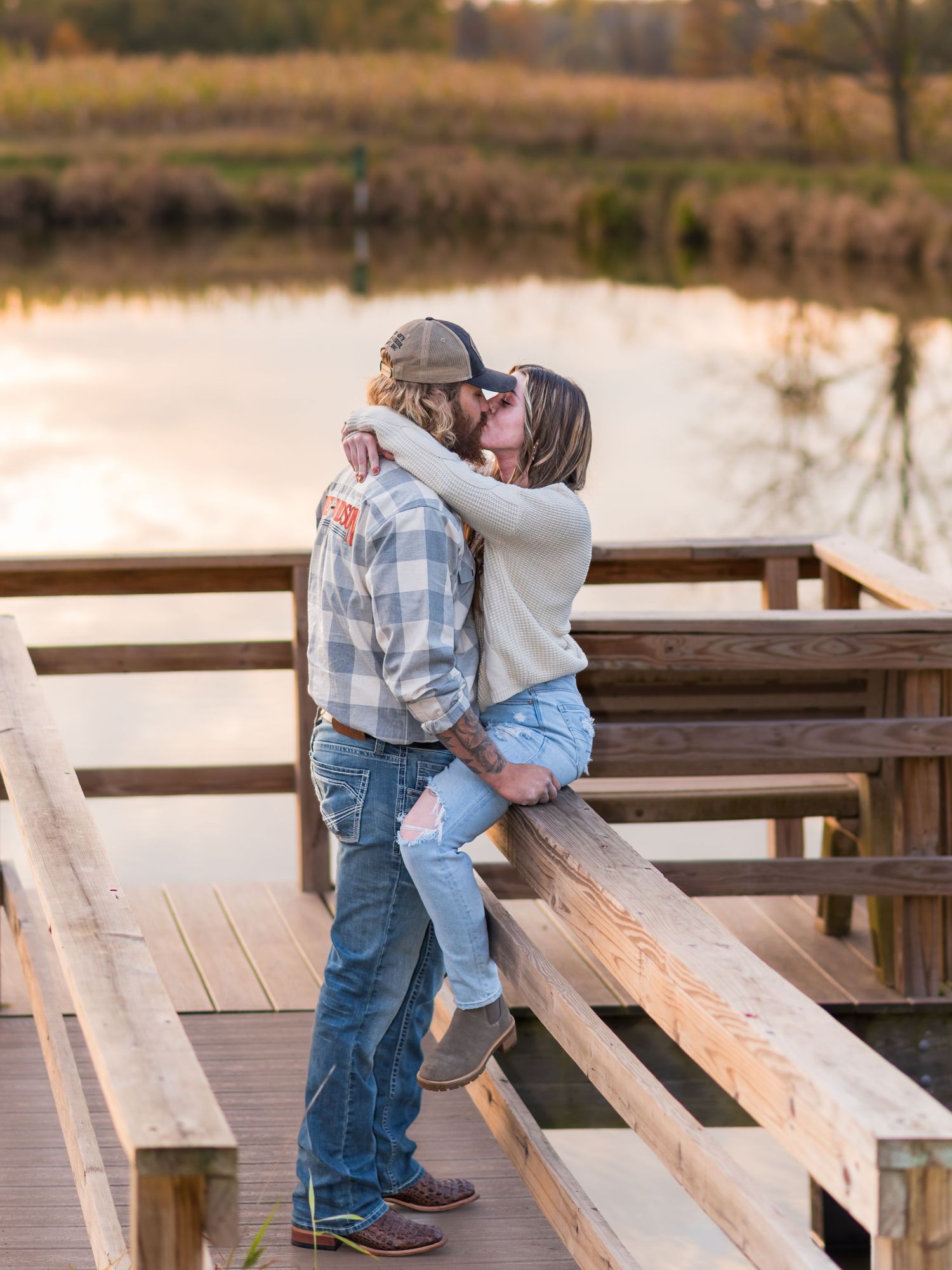 Couple shares tender moment on wooden dock during sunset by lake.