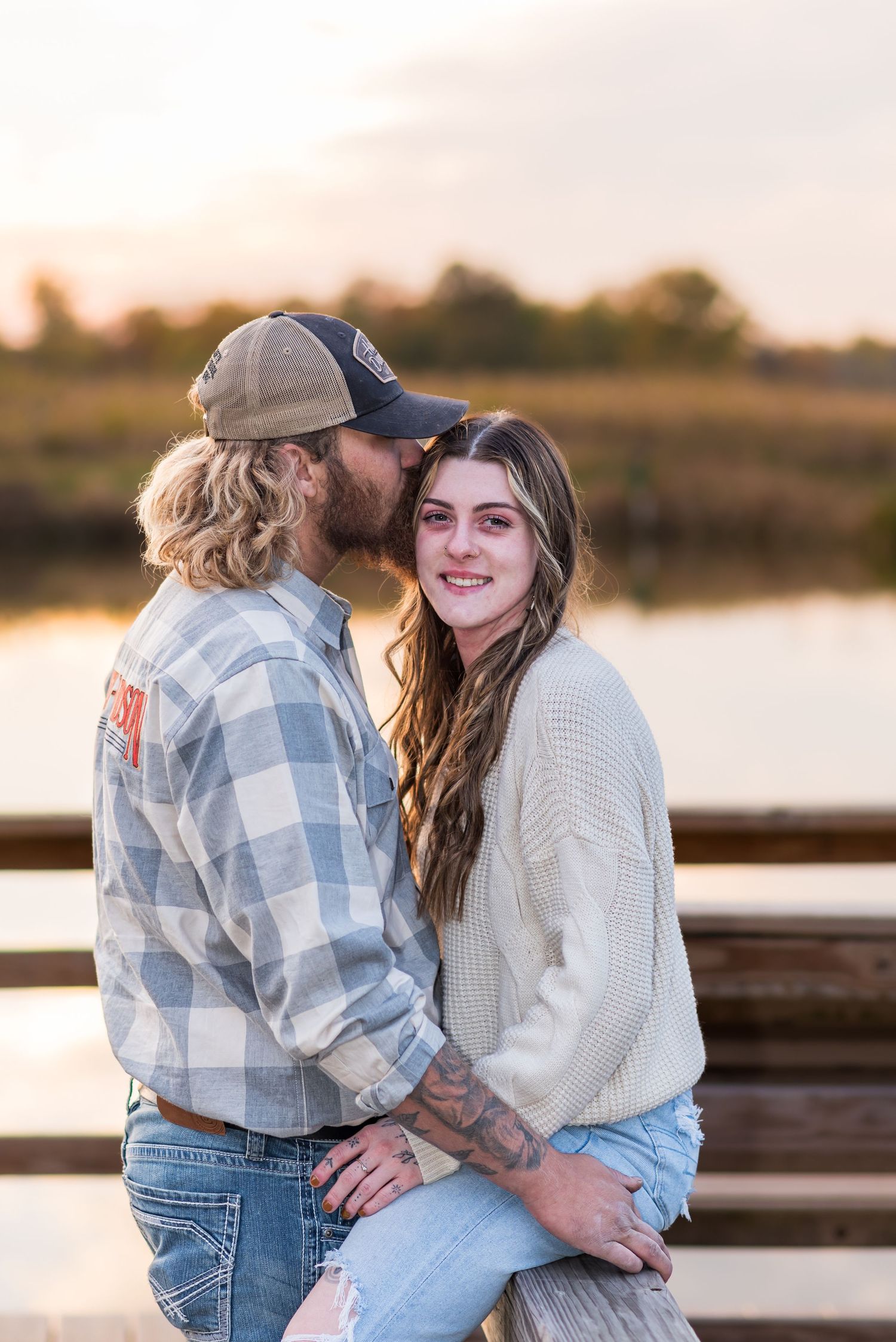 Couple in casual attire embraces by lakeside during sunset.
