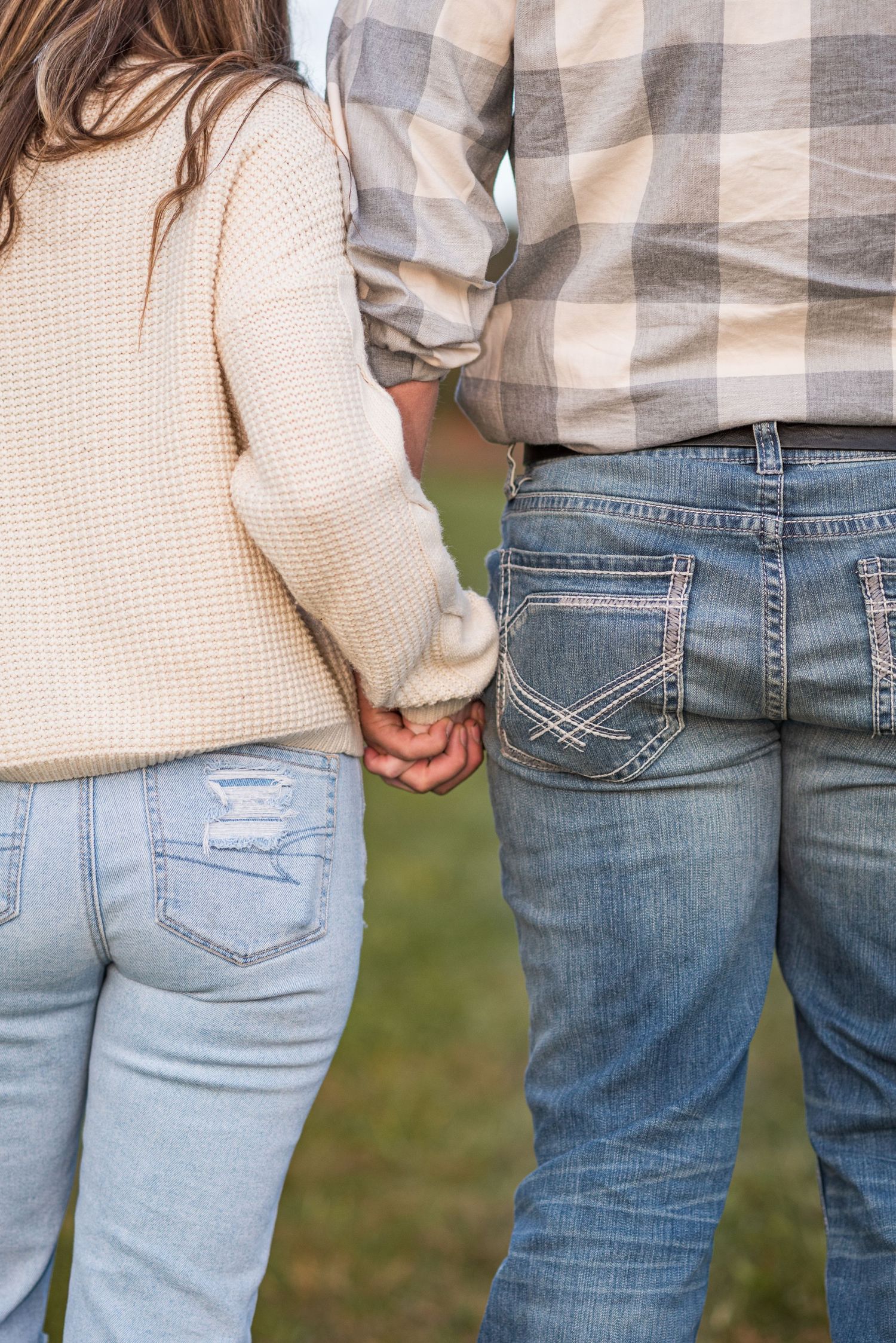 Close-up of couple wearing matching cream sweaters and jeans standing together outdoors.