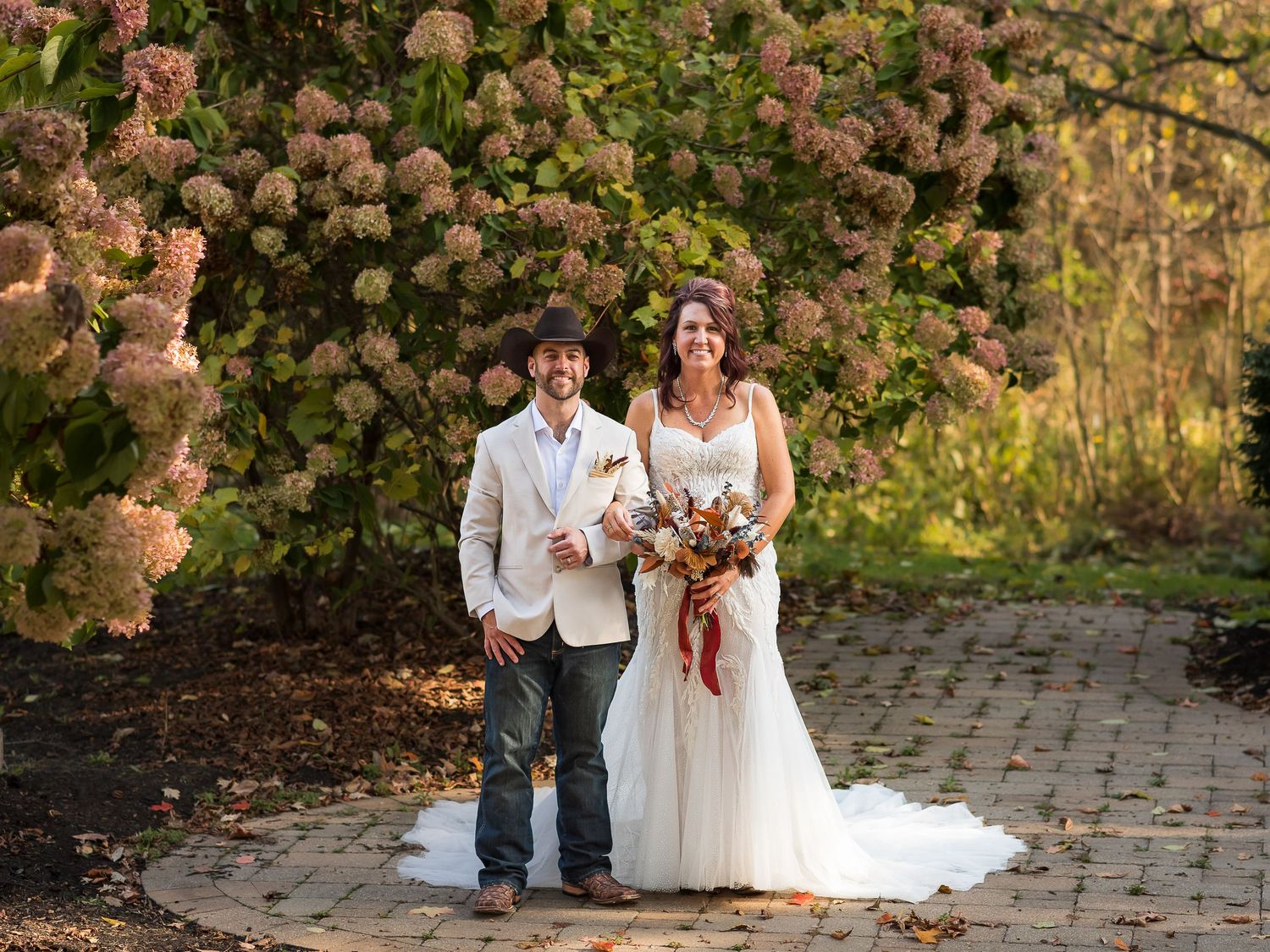 A couple poses together on a stone pathway surrounded by blooming hydrangea bushes.
