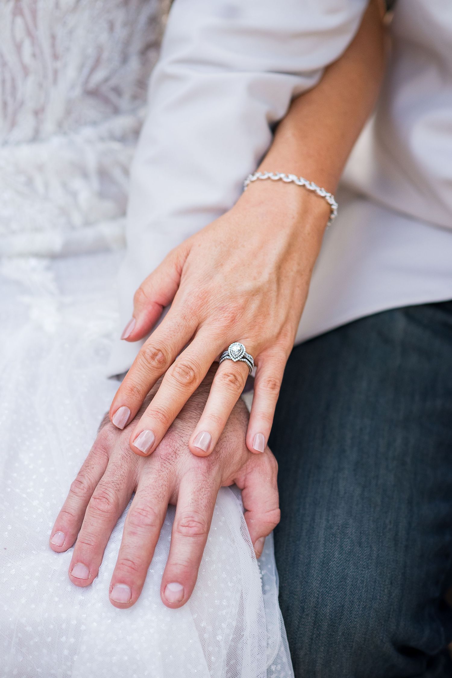 Close-up of hands resting on white lace fabric showing an engagement ring.