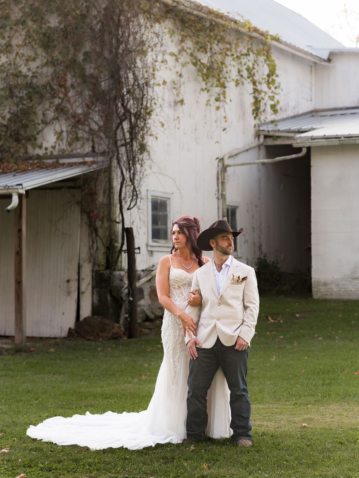 A couple poses together against a white building with ivy growing on the walls.