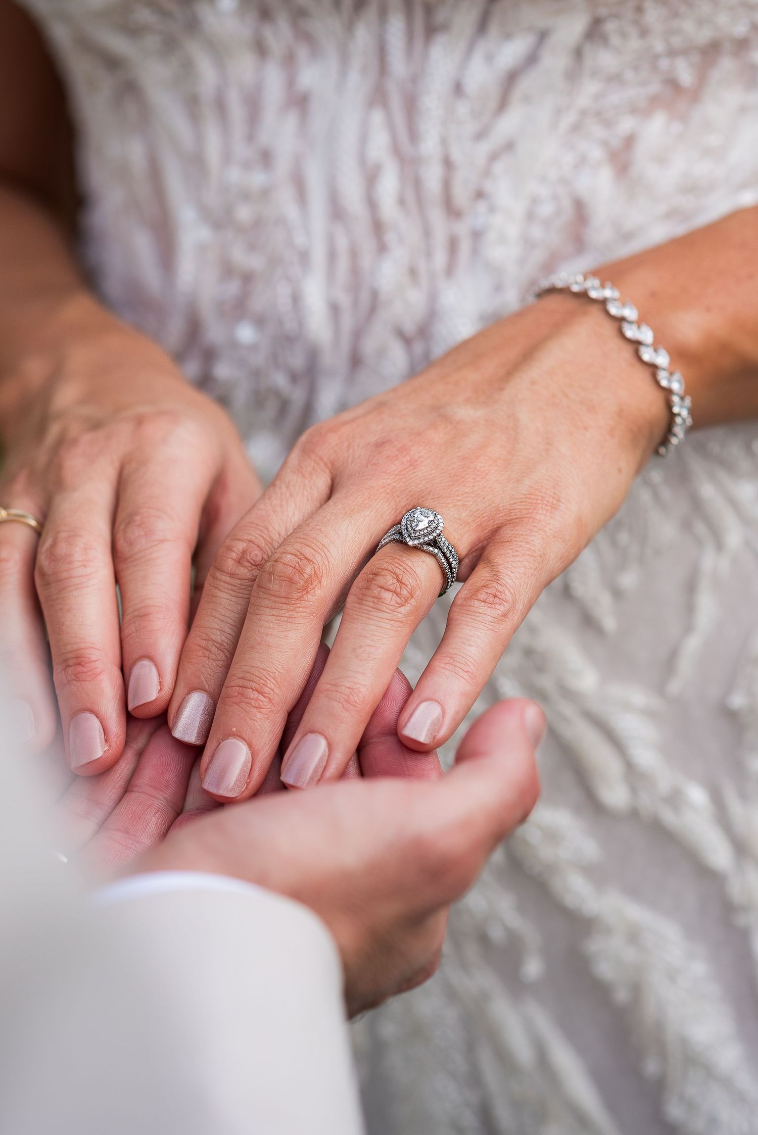 Close-up of hands with engagement rings and delicate manicured nails.