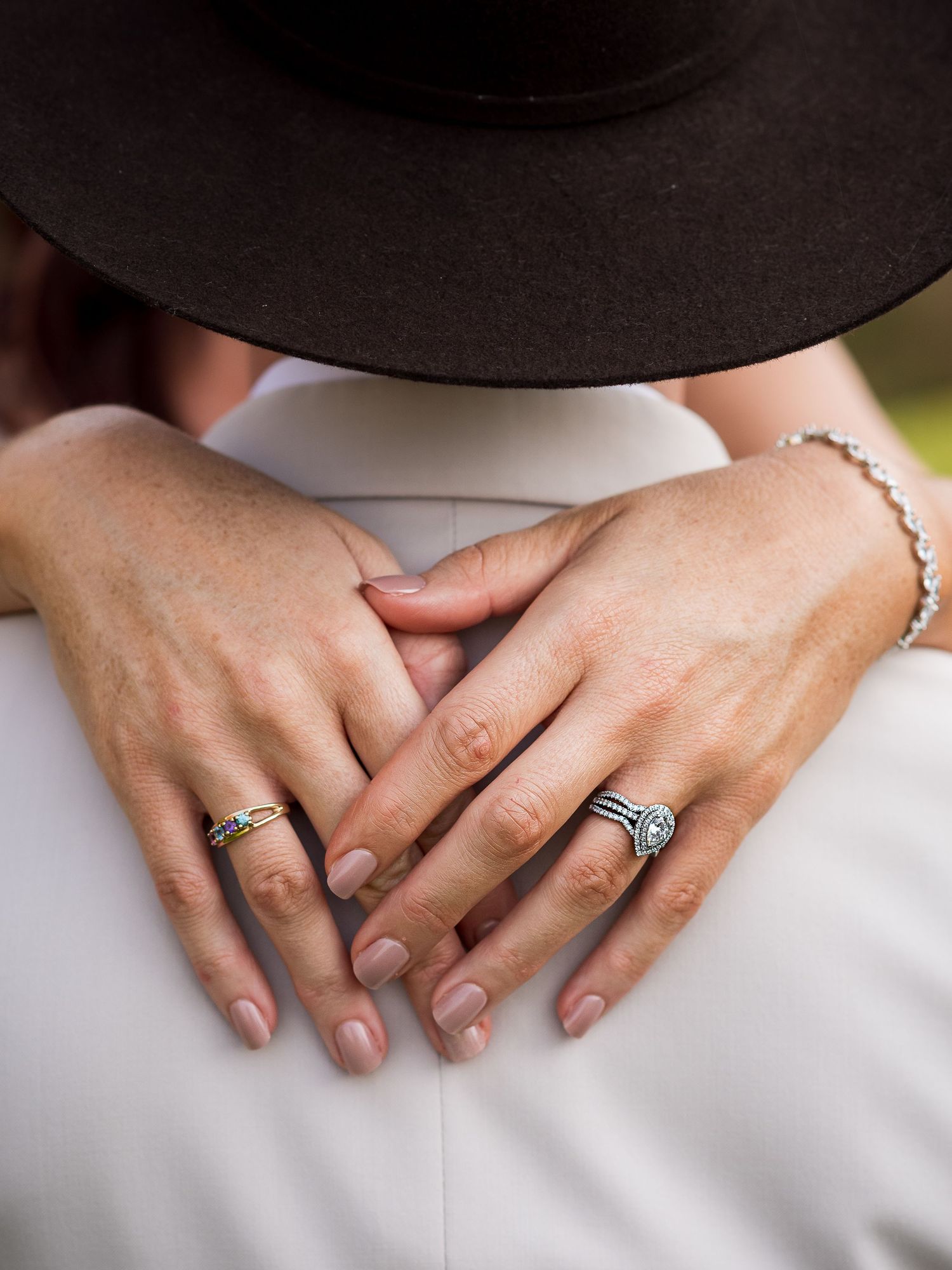 Detailed shot of hands with engagement rings resting on white fabric.