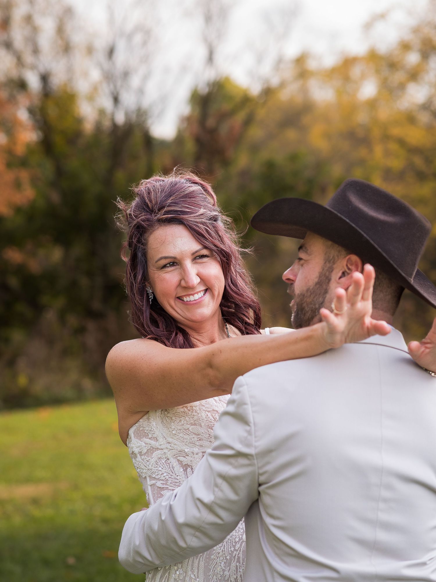 A joyful embrace captured outdoors during autumn with fall foliage in the background.