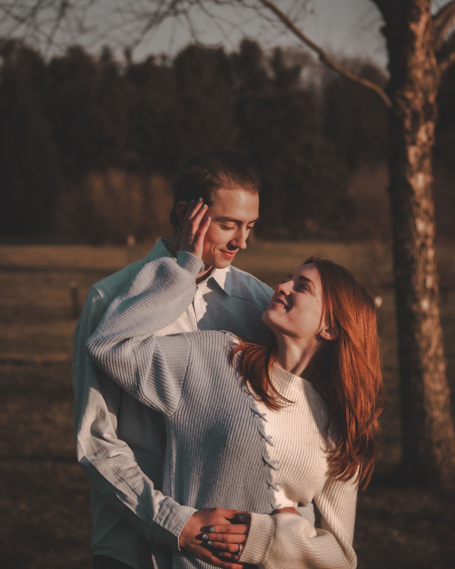 Romantic couple embracing and laughing together at dusk in a rustic outdoor setting.