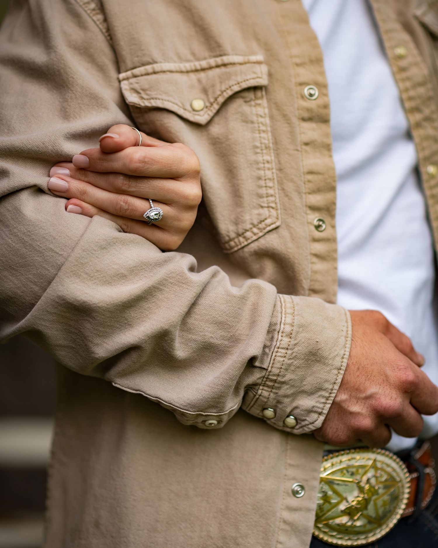 Hands wearing engagement rings shown against khaki and white clothing.