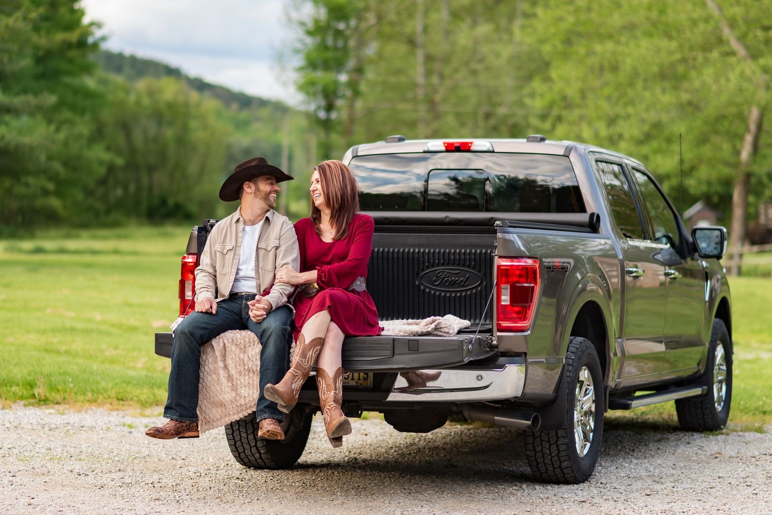 A couple sitting together on the back of a pickup truck in a rural setting.