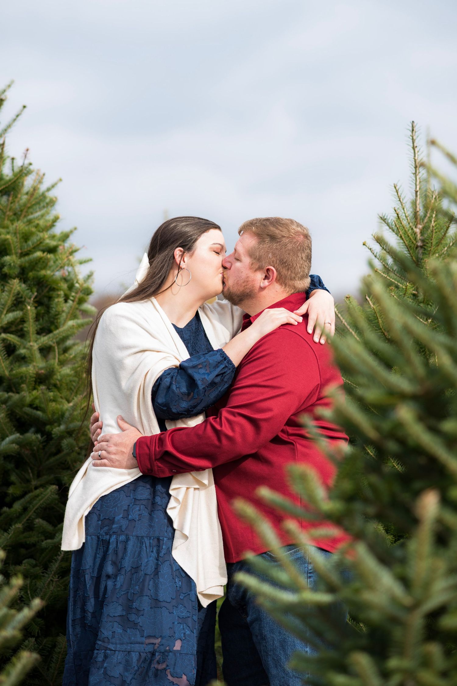 A romantic moment captured at a Christmas tree farm with evergreens in the background.