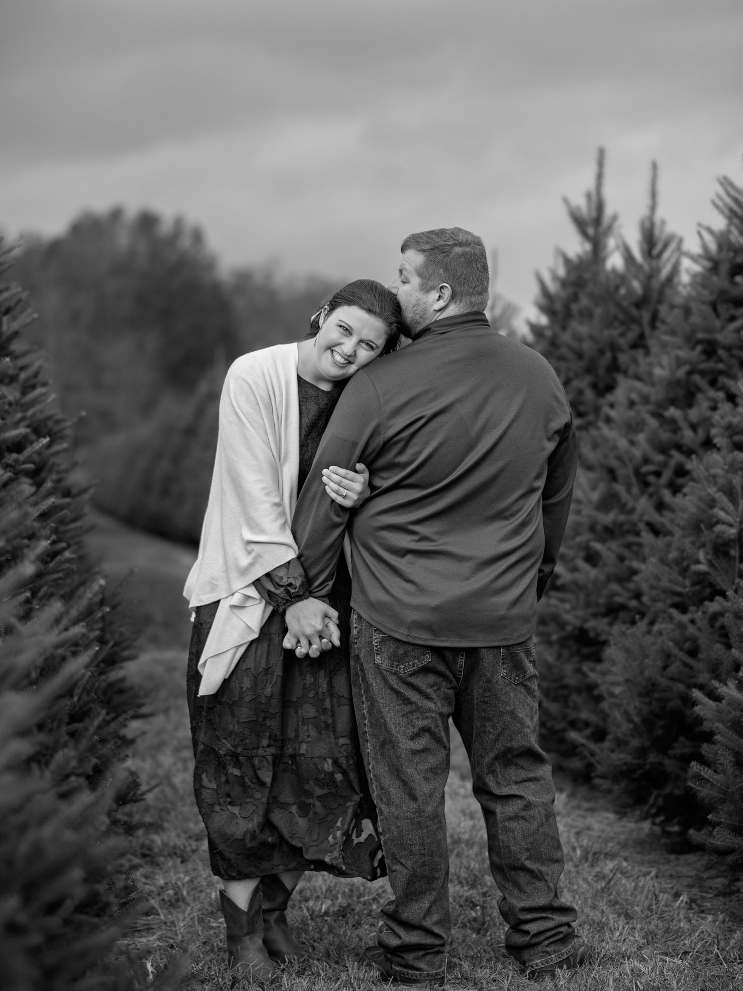 A black and white romantic photoshoot among rows of Christmas trees.