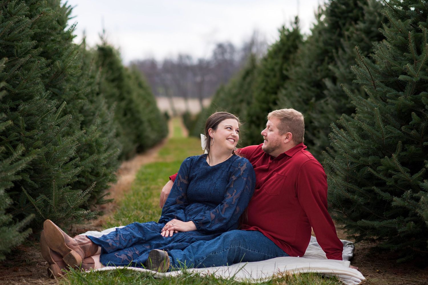A couple sharing intimate moments between rows of evergreen trees at a Christmas tree farm.