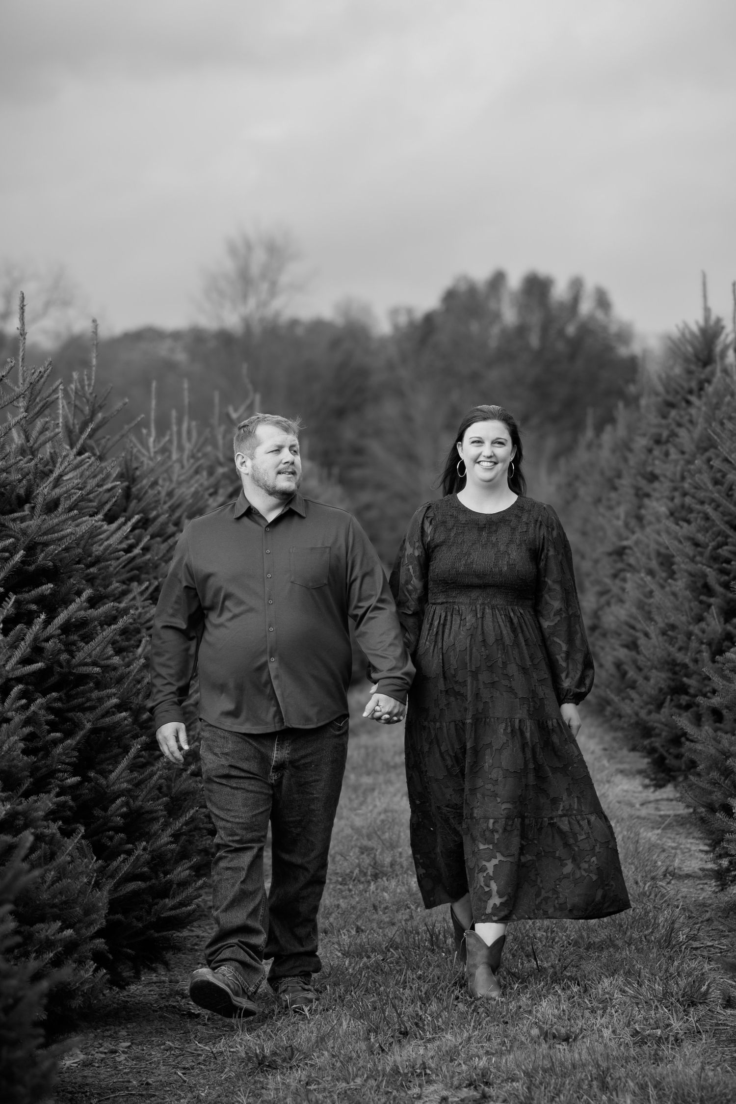 A black and white photograph of couples walking through rows of evergreen Christmas trees.