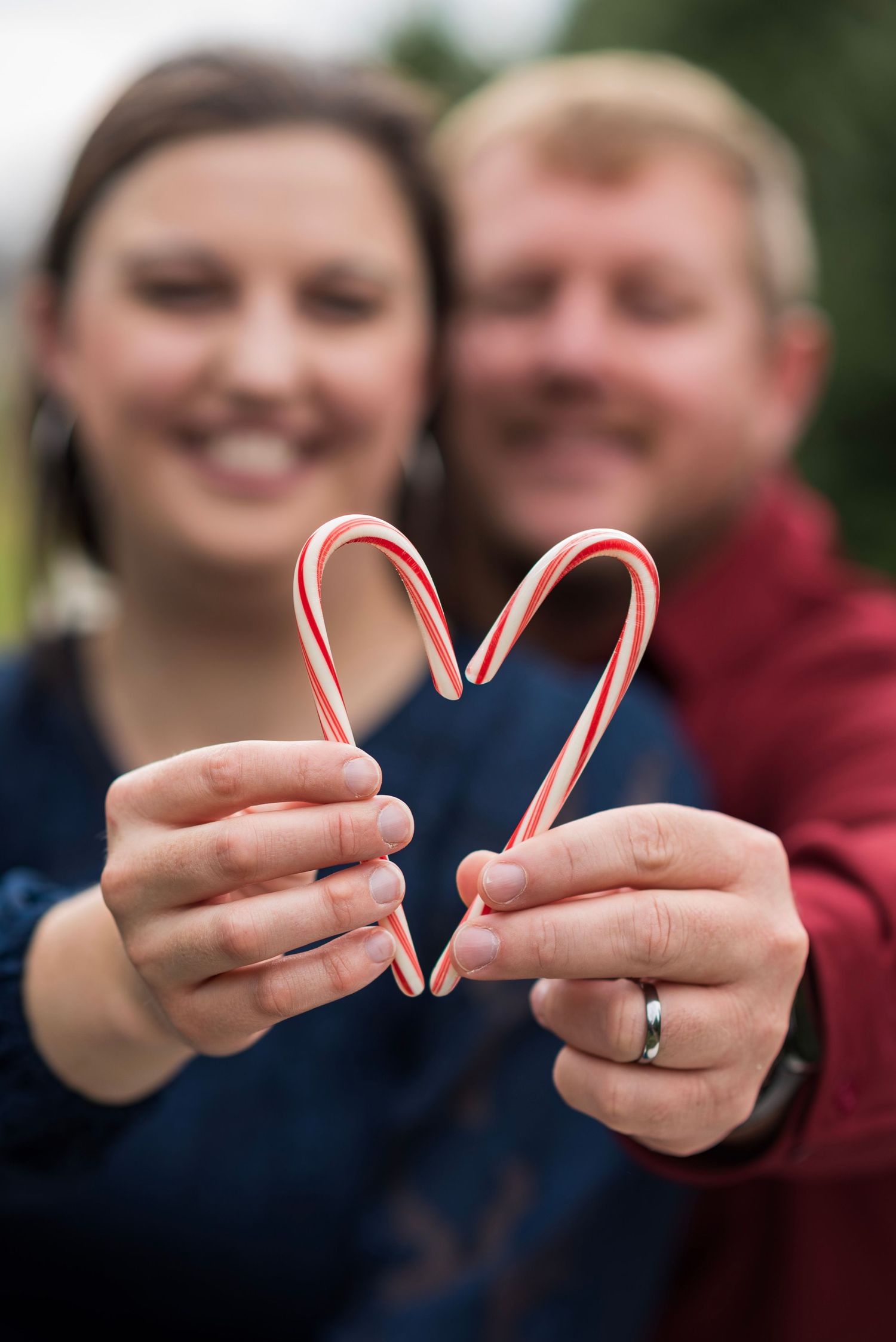 Hands holding candy canes forming heart shapes against a blurred festive background.