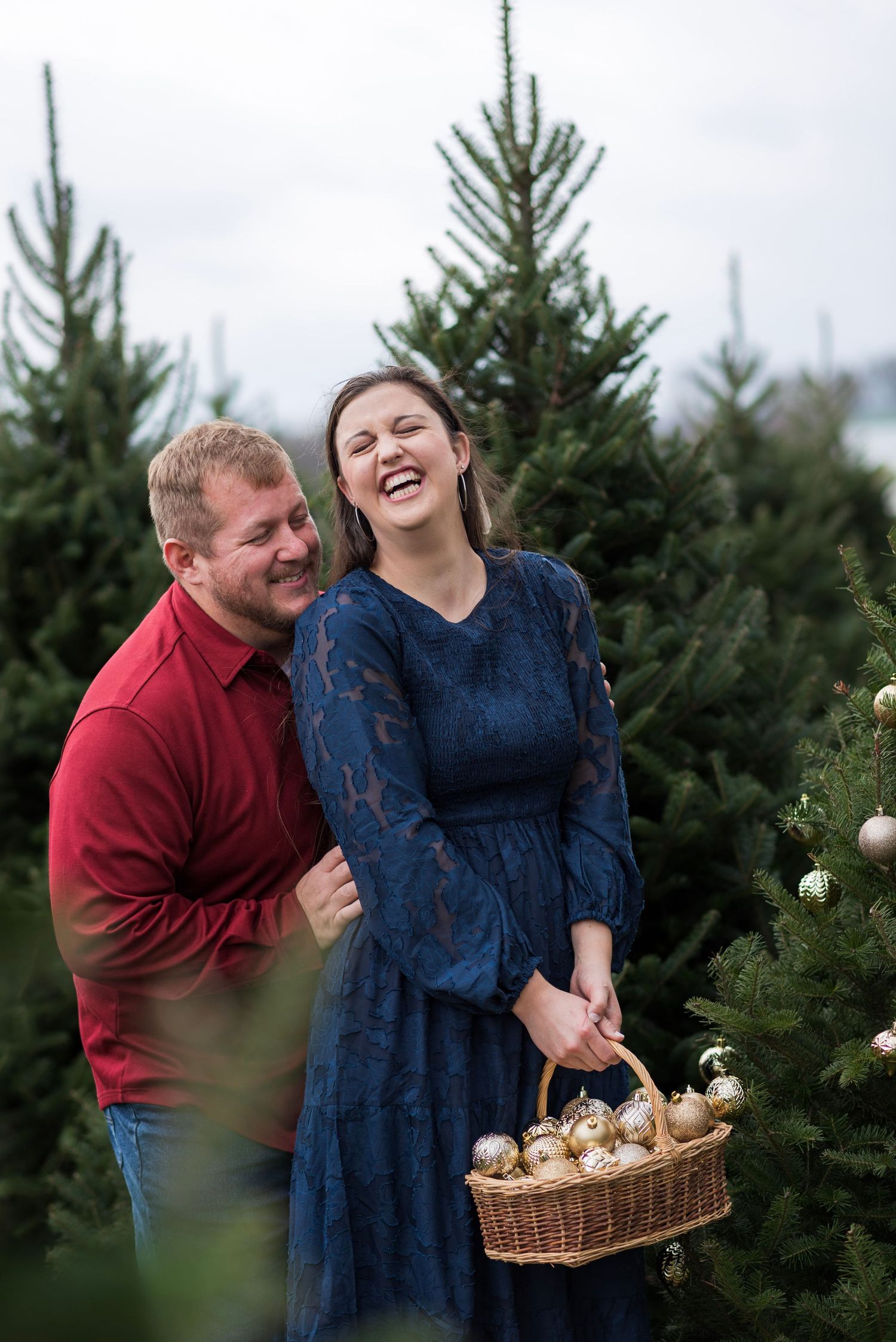 A joyful moment at a Christmas tree farm with a basket of golden ornaments.