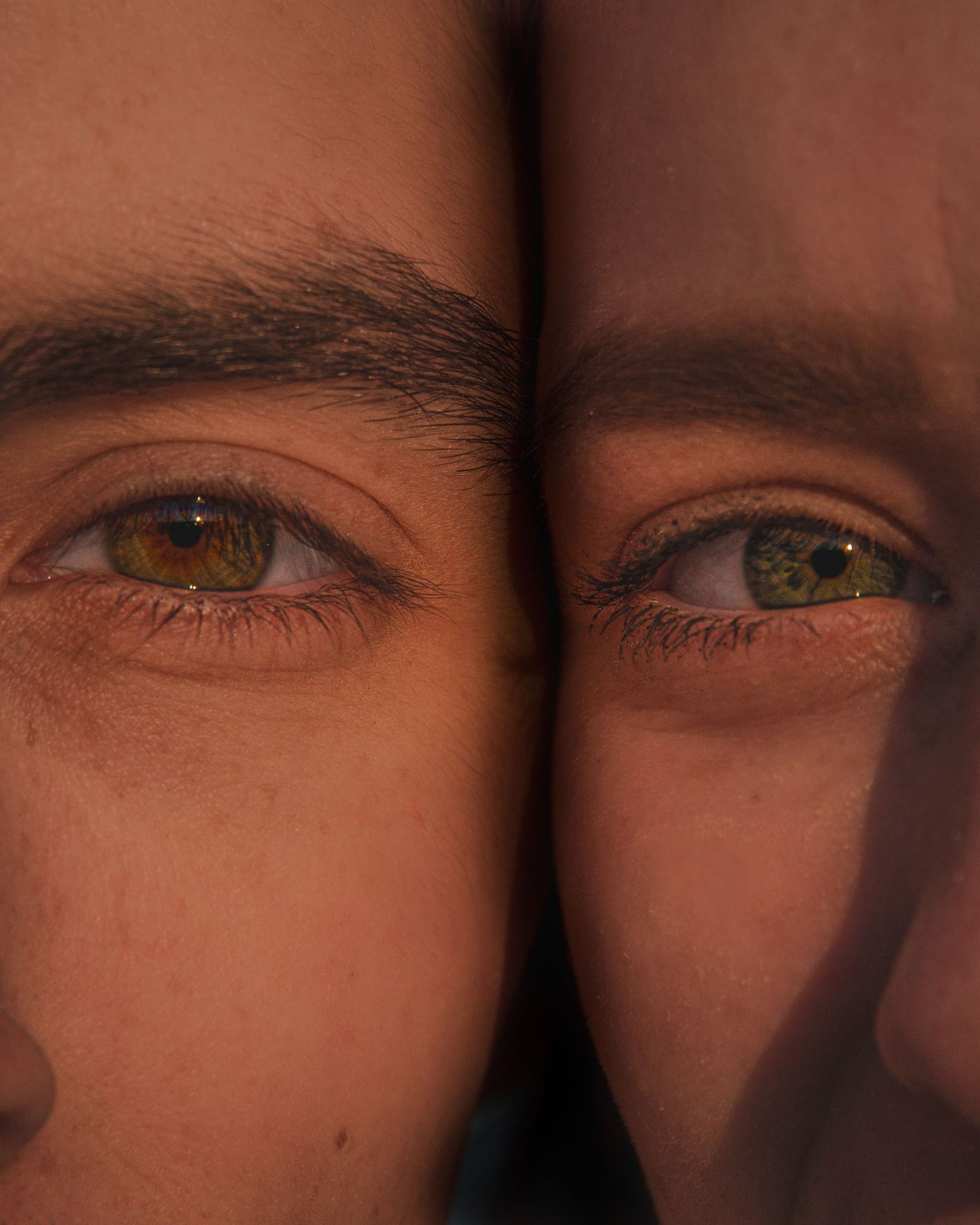 Close-up artistic photo of two different colored eyes side by side in warm lighting.