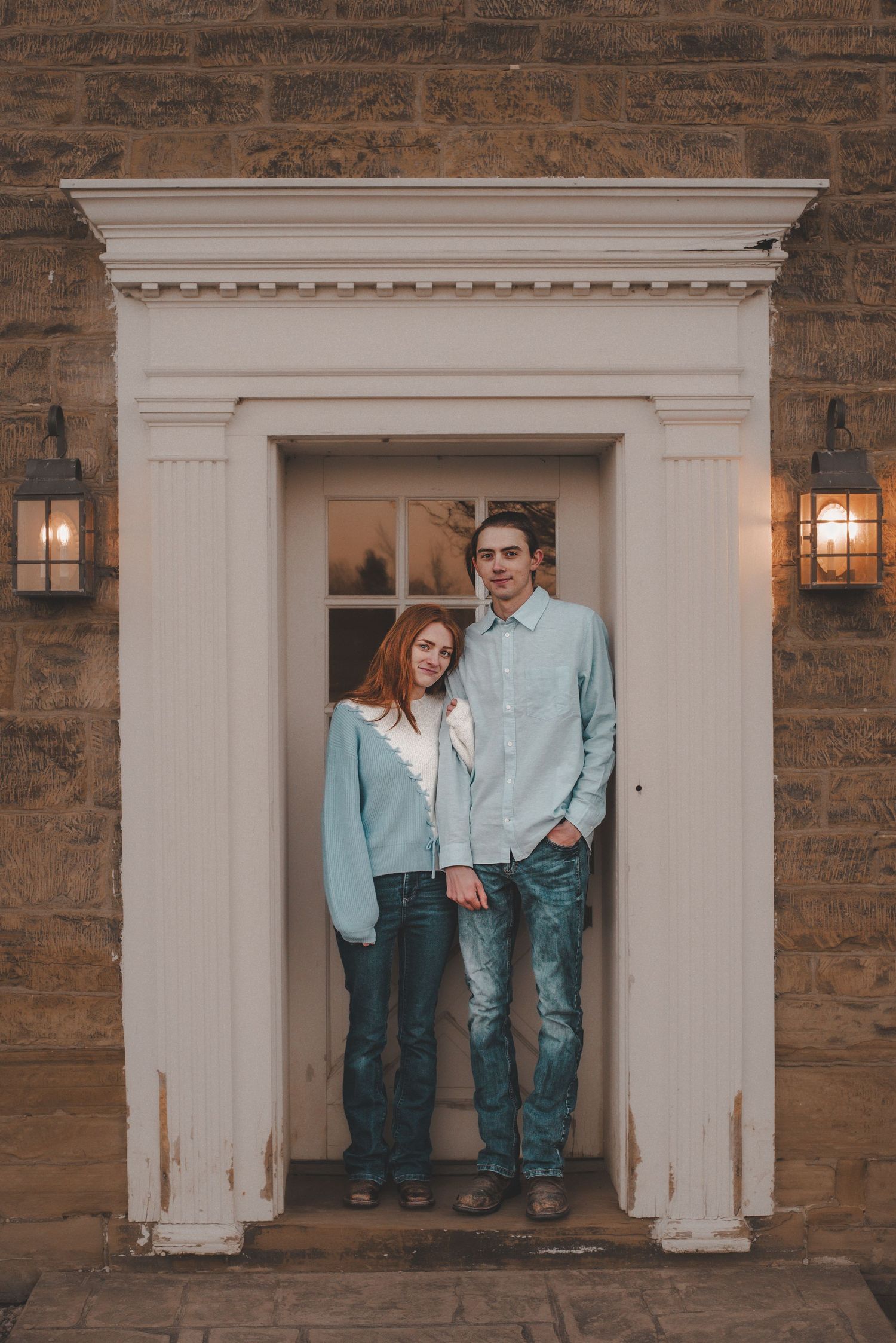 Couple in matching blue outfits standing in an elegant white doorway with wall sconces.