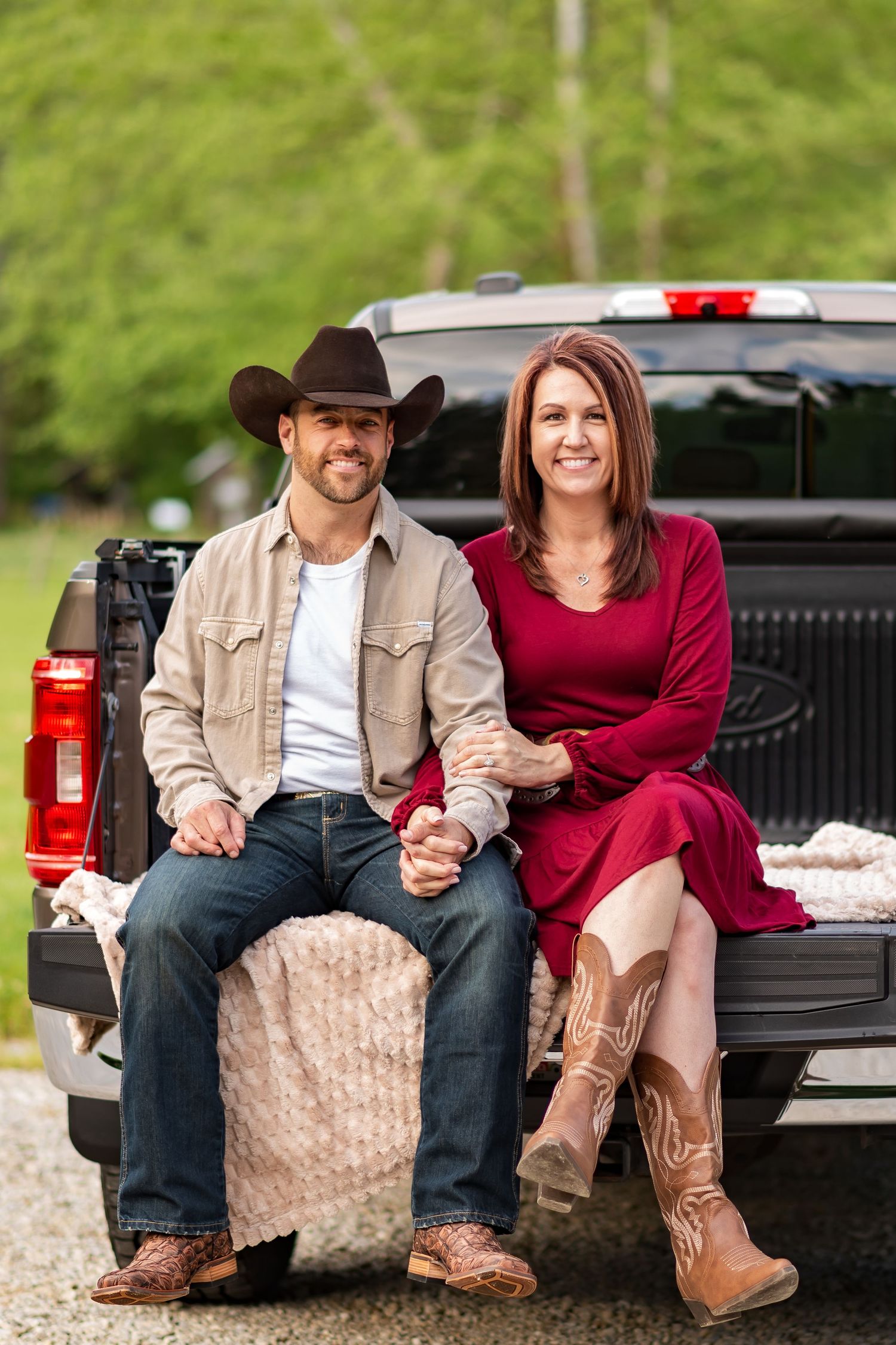 A couple in western boots sitting together on the tailgate of a black pickup truck.