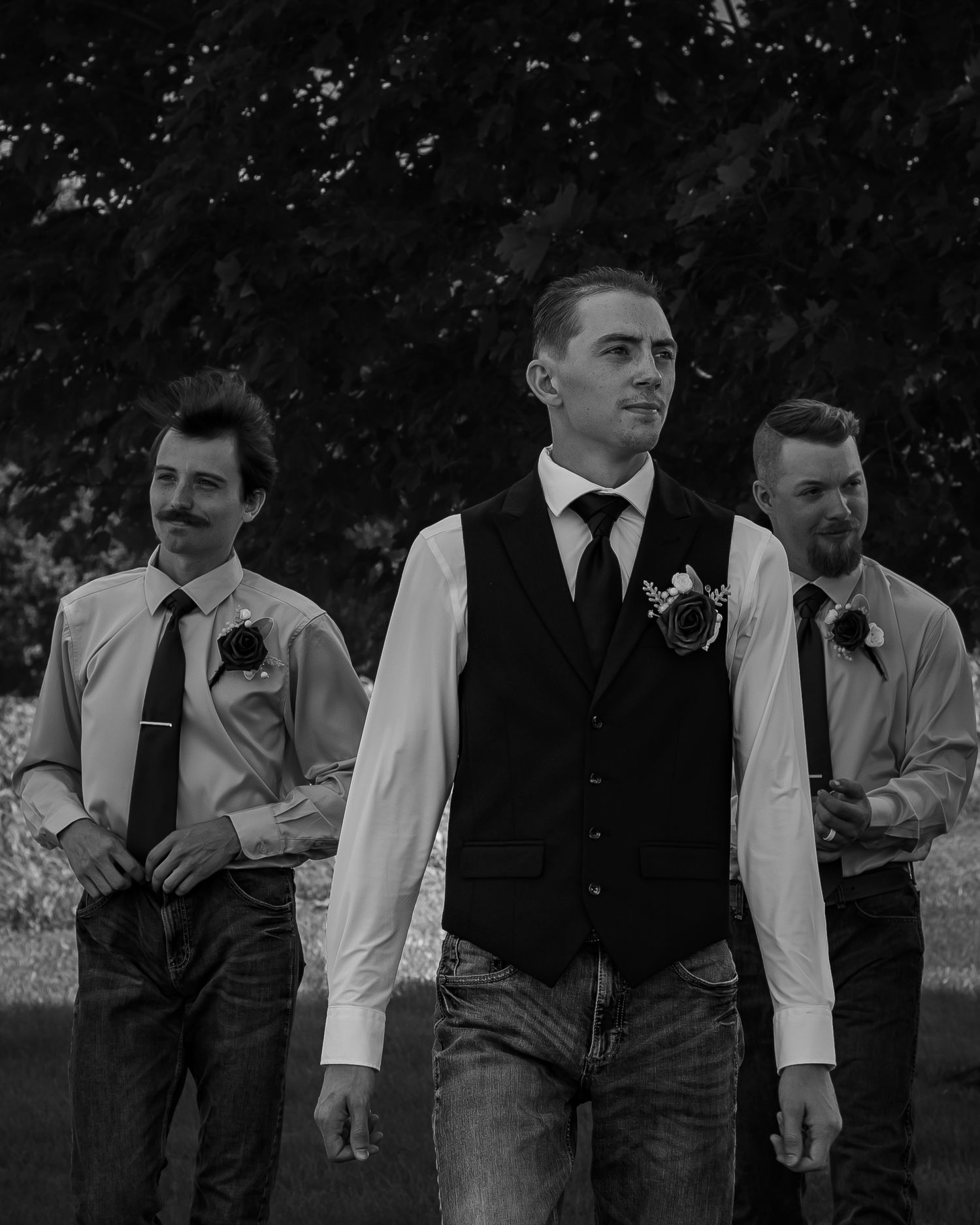 Three groomsmen in formal attire standing together outdoors for wedding photos.