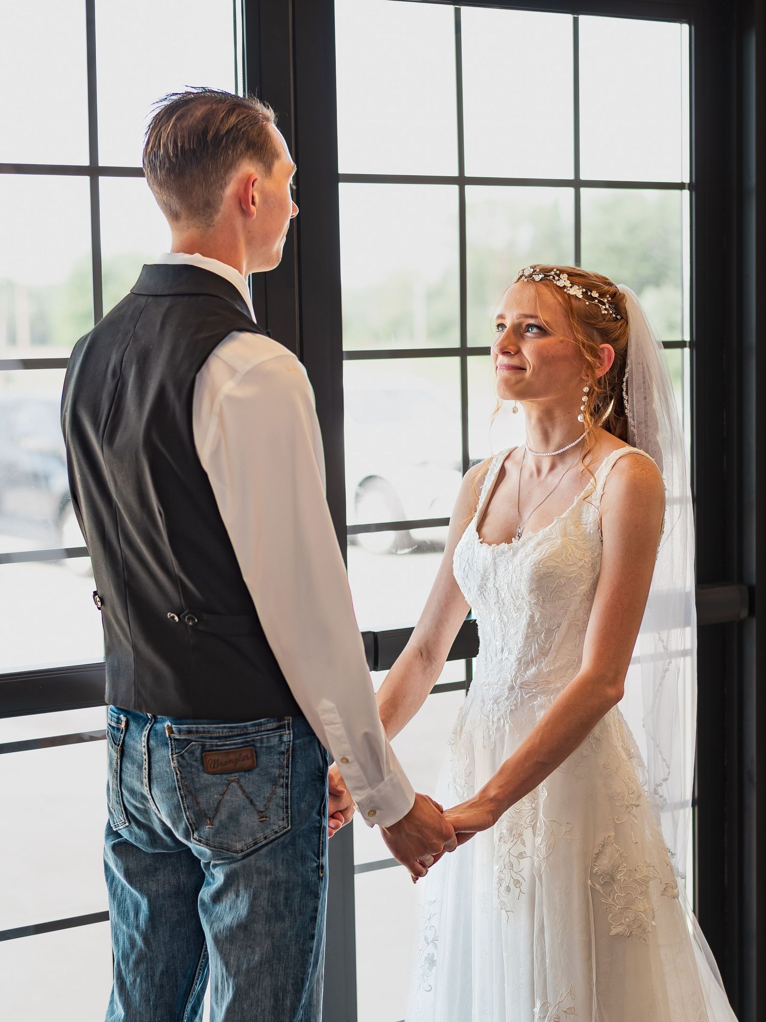 Couple holding hands by large windows during intimate wedding ceremony.