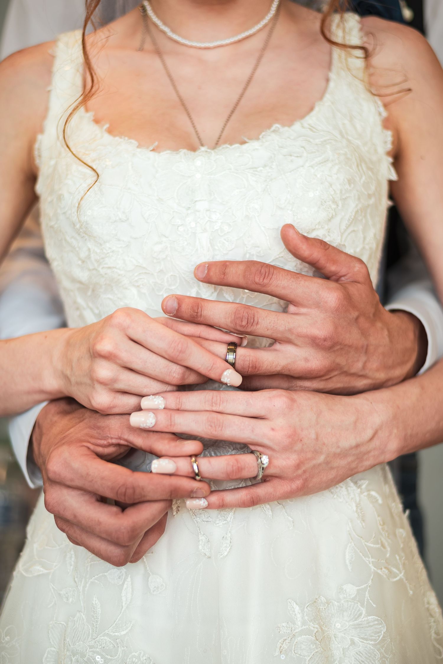 Close-up of hands with wedding rings on white lace wedding dress.