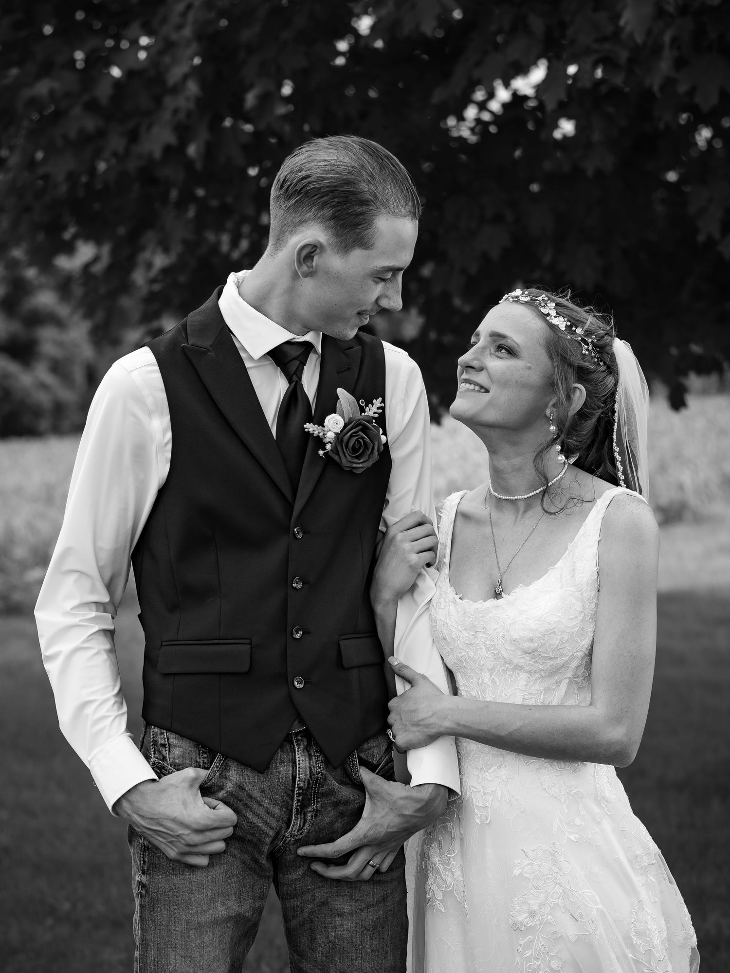 A romantic black and white portrait of newlyweds in casual formal attire outdoors.