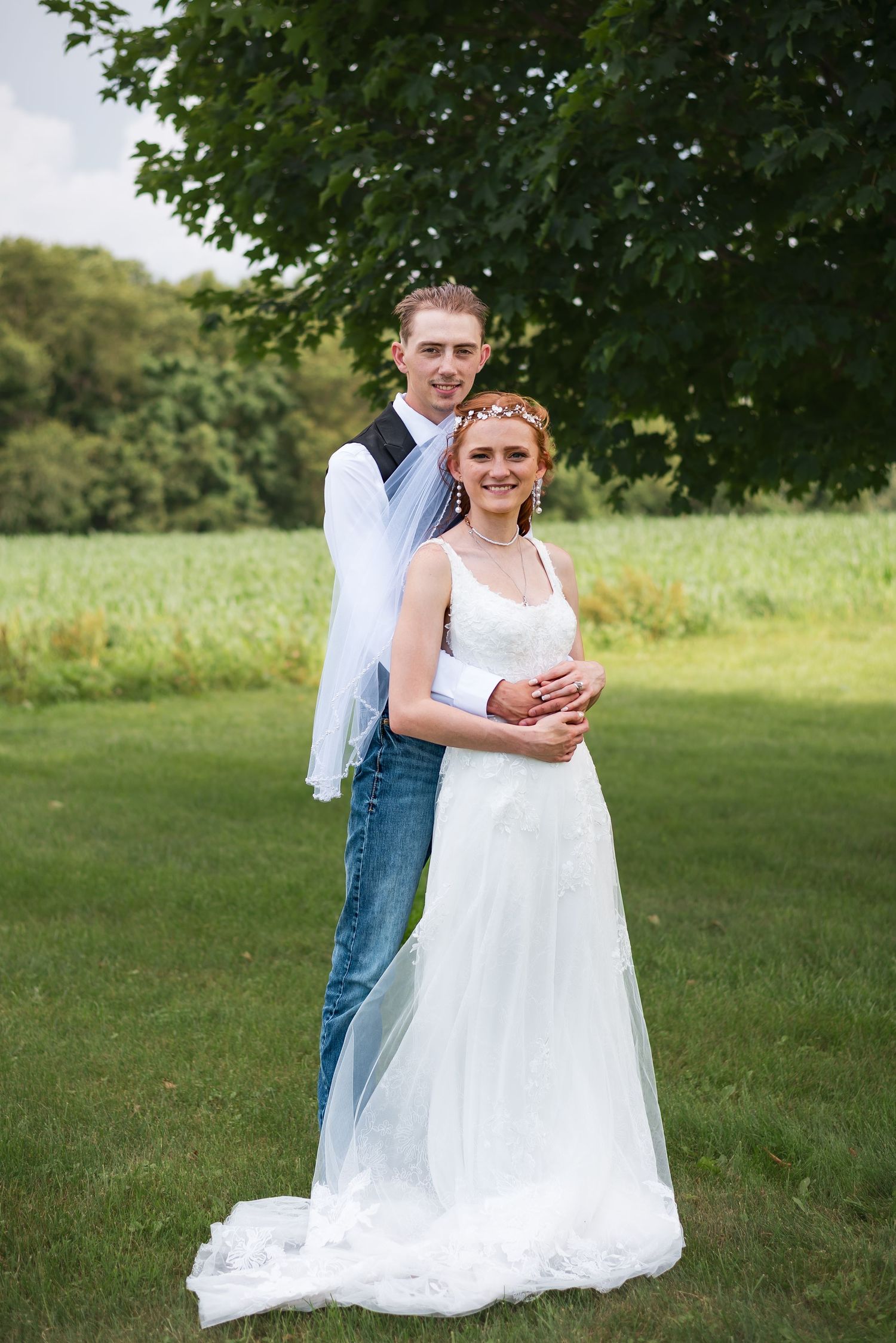 A couple poses for their wedding portrait in a lush green outdoor setting.