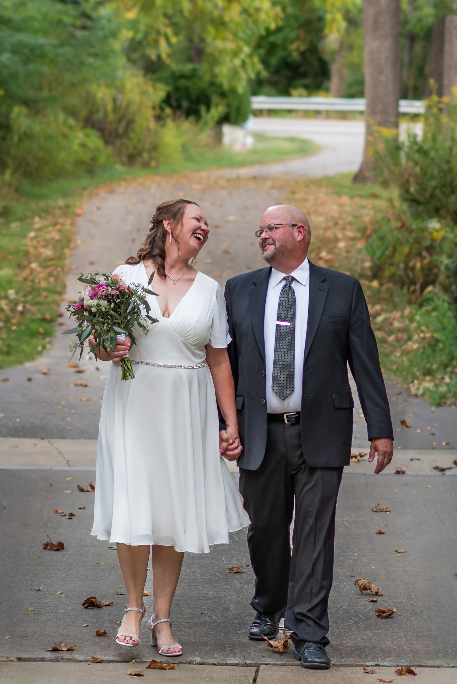 Couple walking hand in hand along autumn path wearing formal dress and suit.