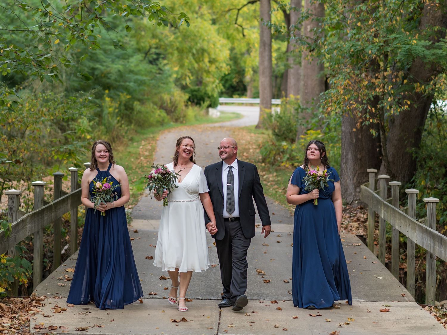 Wedding party in navy blue dresses and formal attire poses on wooden walkway.