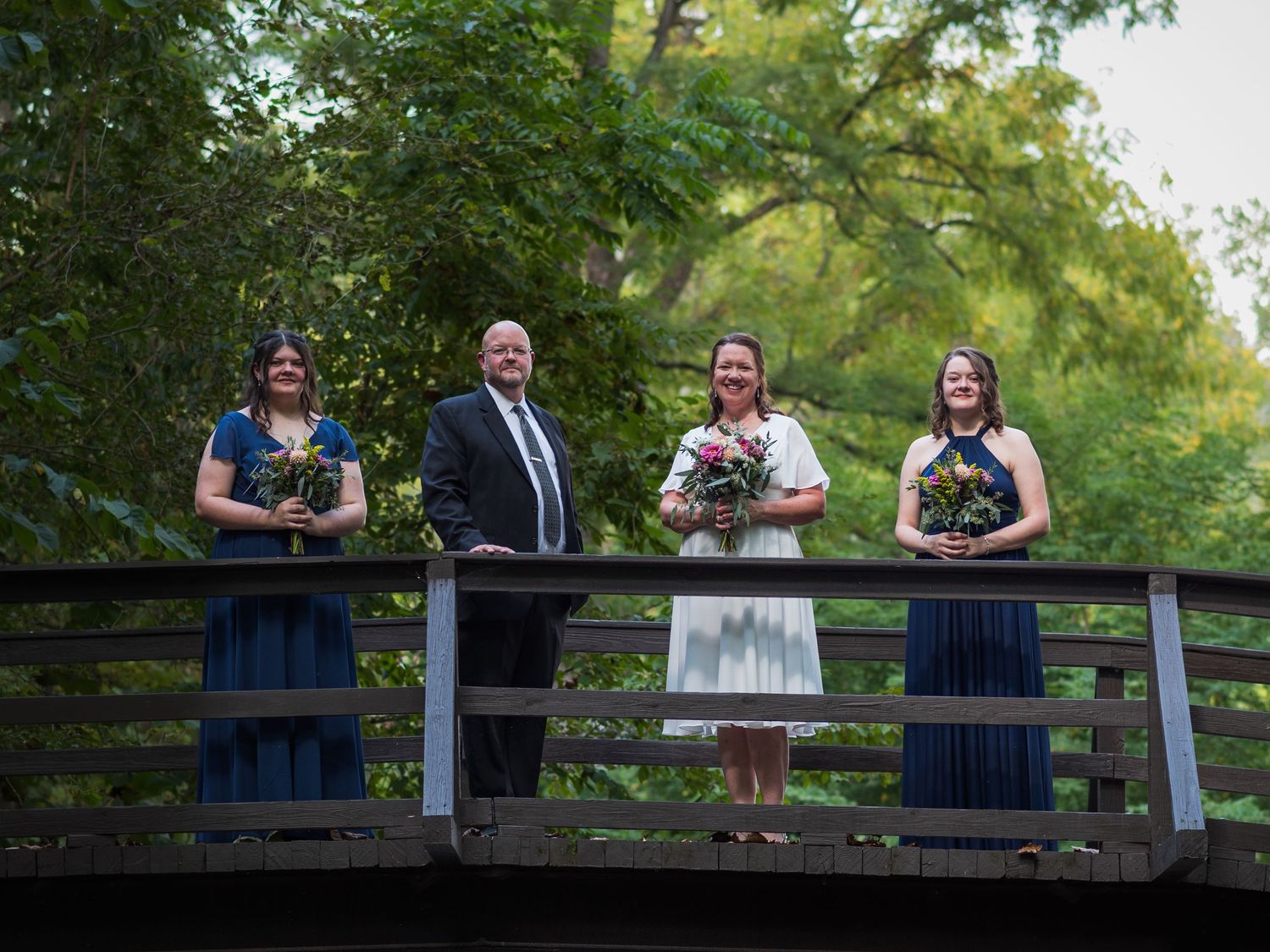 Wedding party members stand on a wooden bridge for a group photo.