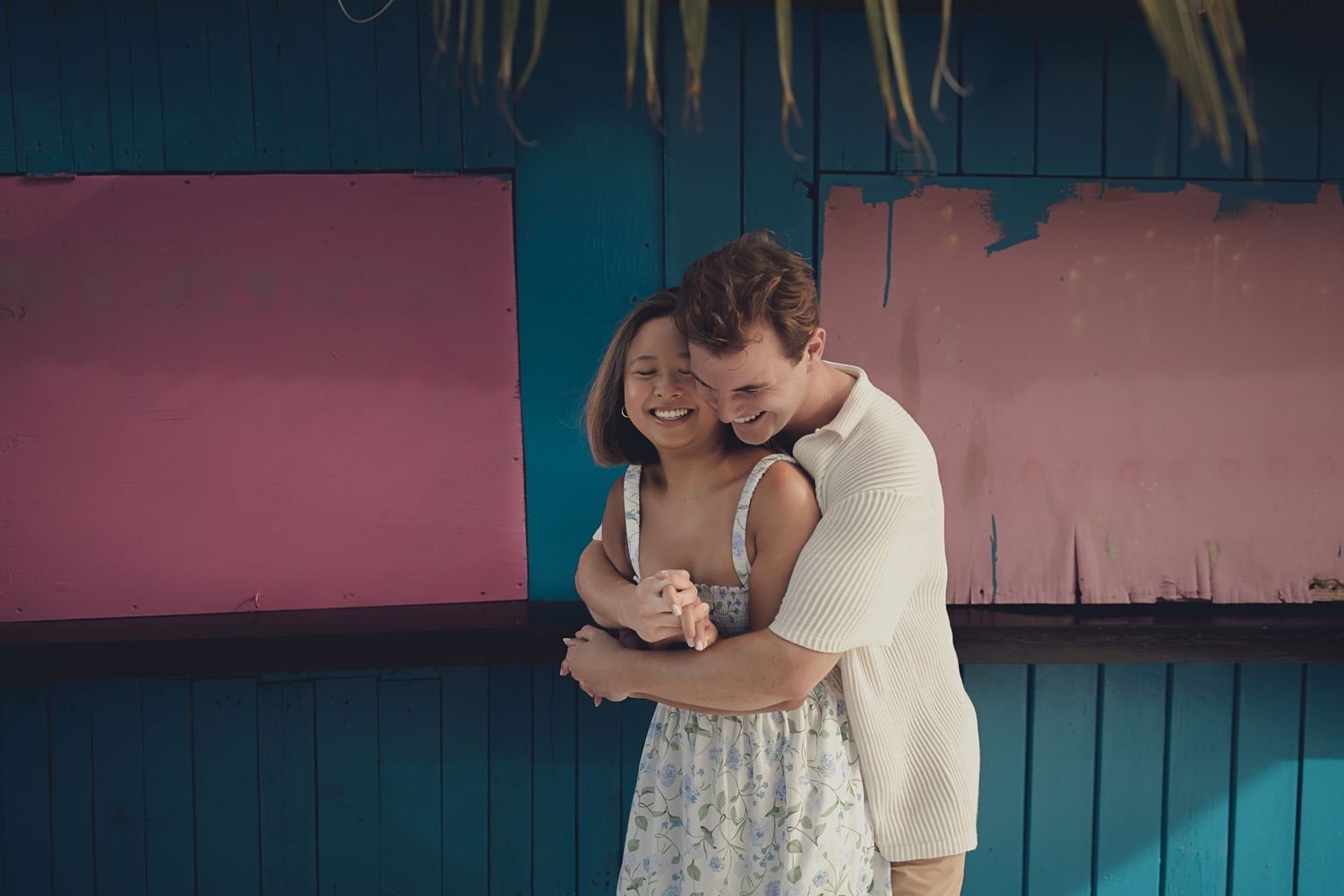 A couple in wedding attire shares romantic moments together during a photo session against a teal wall background.