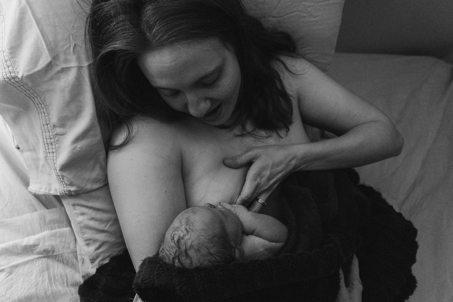 A tender moment captured in black and white as a mother nurses her newborn baby while resting in bed.